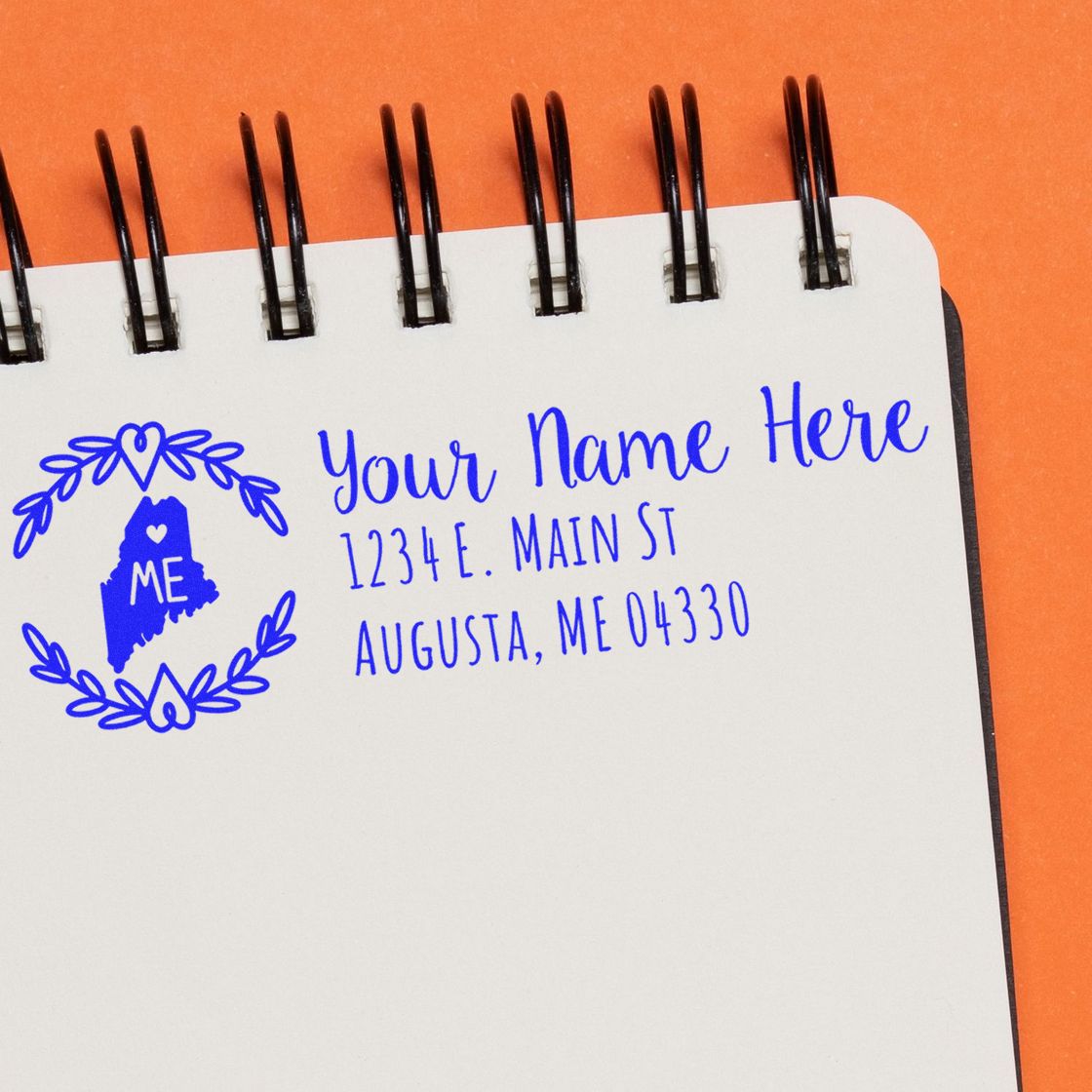 PSI Pre-Inked Maine State Customized Address Stamp on a notepad with a blue design featuring a heart and ME inside a state outline, showcasing a sample address in Augusta, ME.