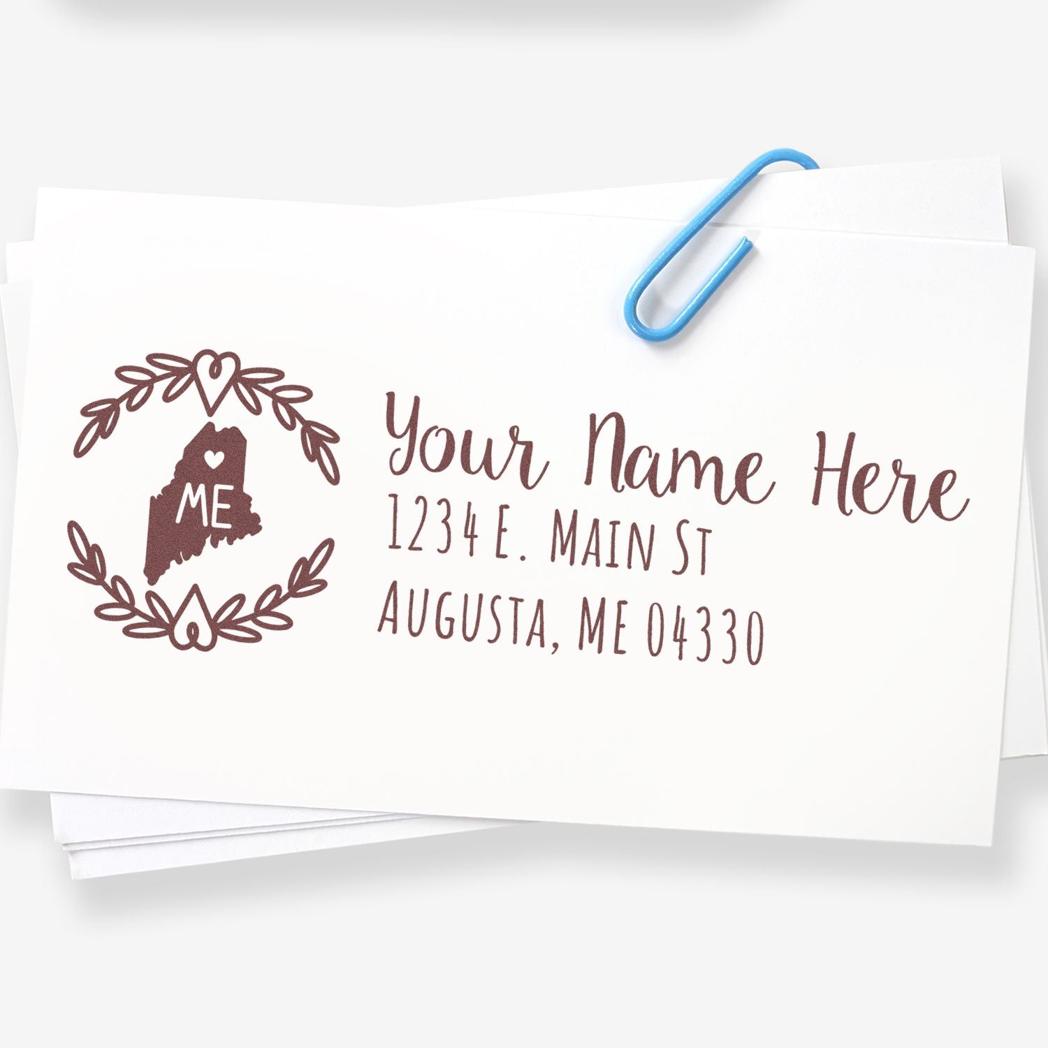 Maine State Custom Return Address Stamp on white paper, featuring a heart design with ME inside the state outline, personalized with name and address, clipped with a blue paperclip.