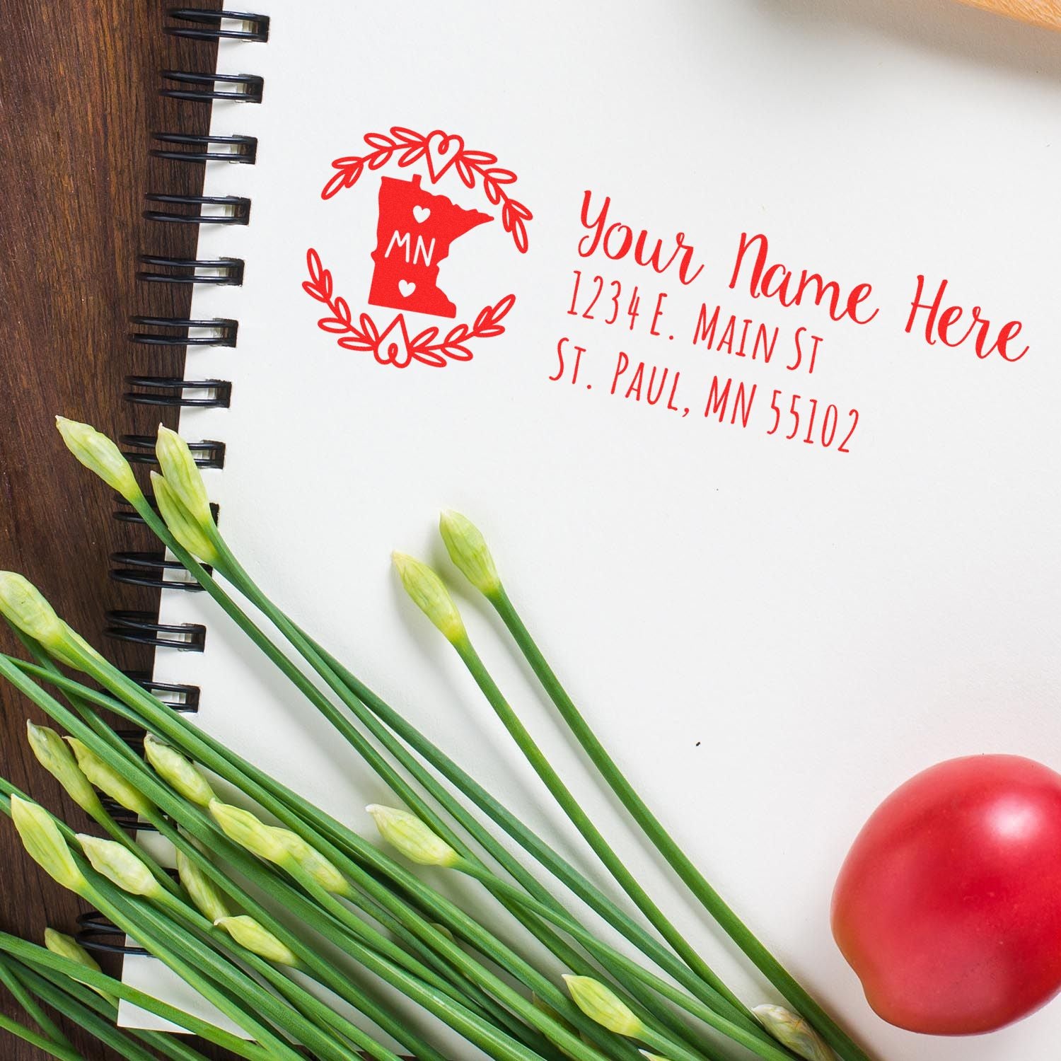 Minnesota State Custom Return Address Stamp in red ink on white paper, featuring a state outline with floral accents. Surrounded by green stems and a red tomato on a wooden surface.