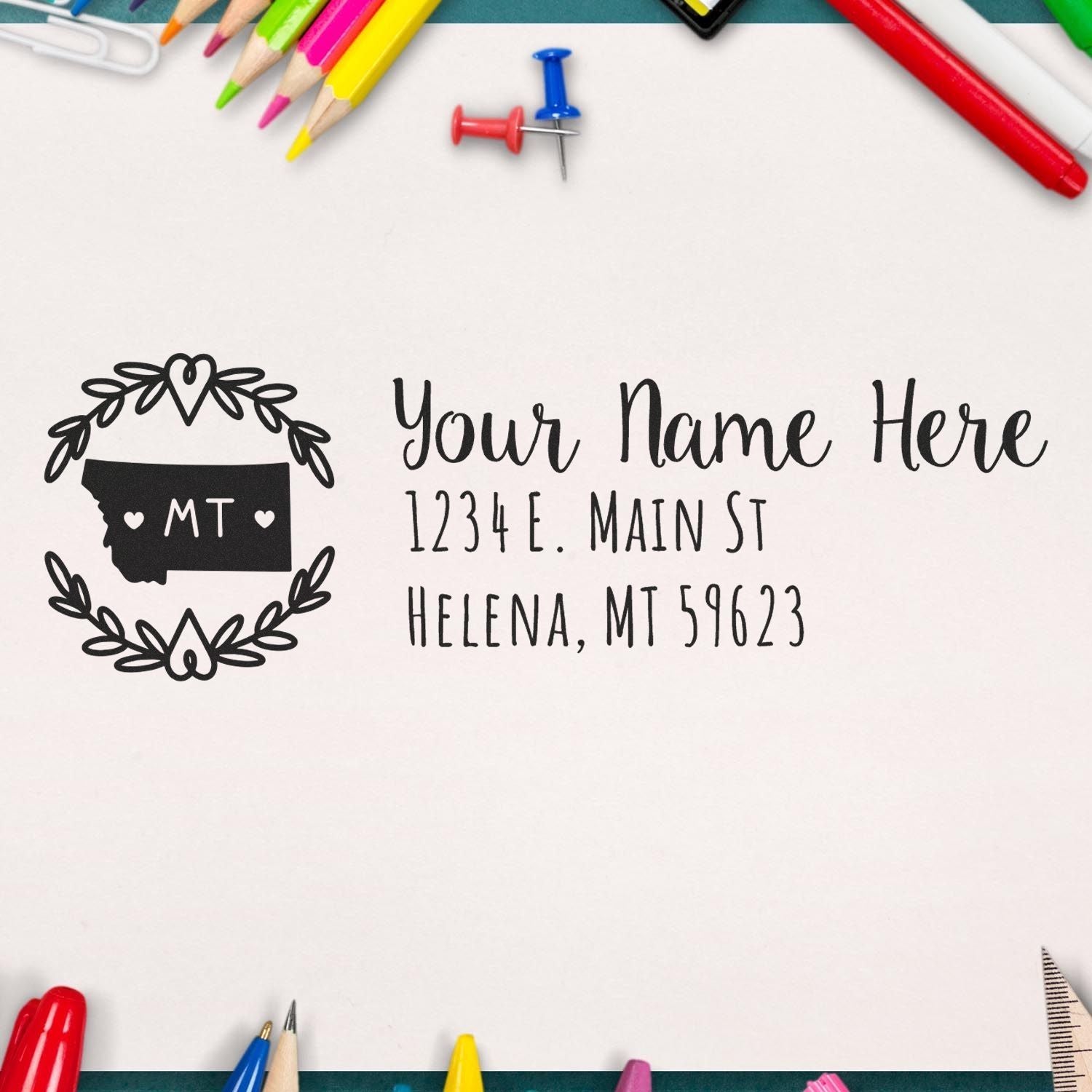 Montana State Custom Return Address Stamp on a white paper surrounded by colorful stationery, featuring a decorative state outline with hearts and personalized address text.