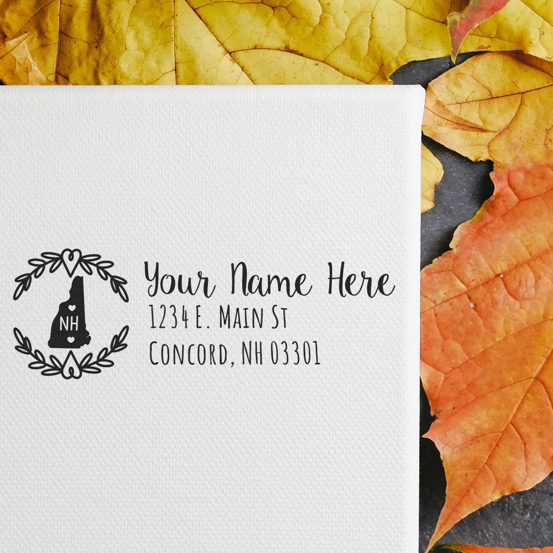 Self-Inking State Wreath of New Hampshire Address Stamp on white paper, surrounded by autumn leaves. Features a wreath design with NH inside, and customizable address text.