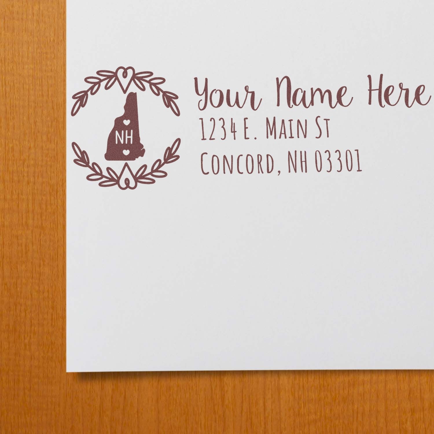 PSI Pre-Inked New Hampshire State Customized Address Stamp on white paper, featuring a decorative NH state outline with hearts, personalized address, and elegant font on a wooden surface.