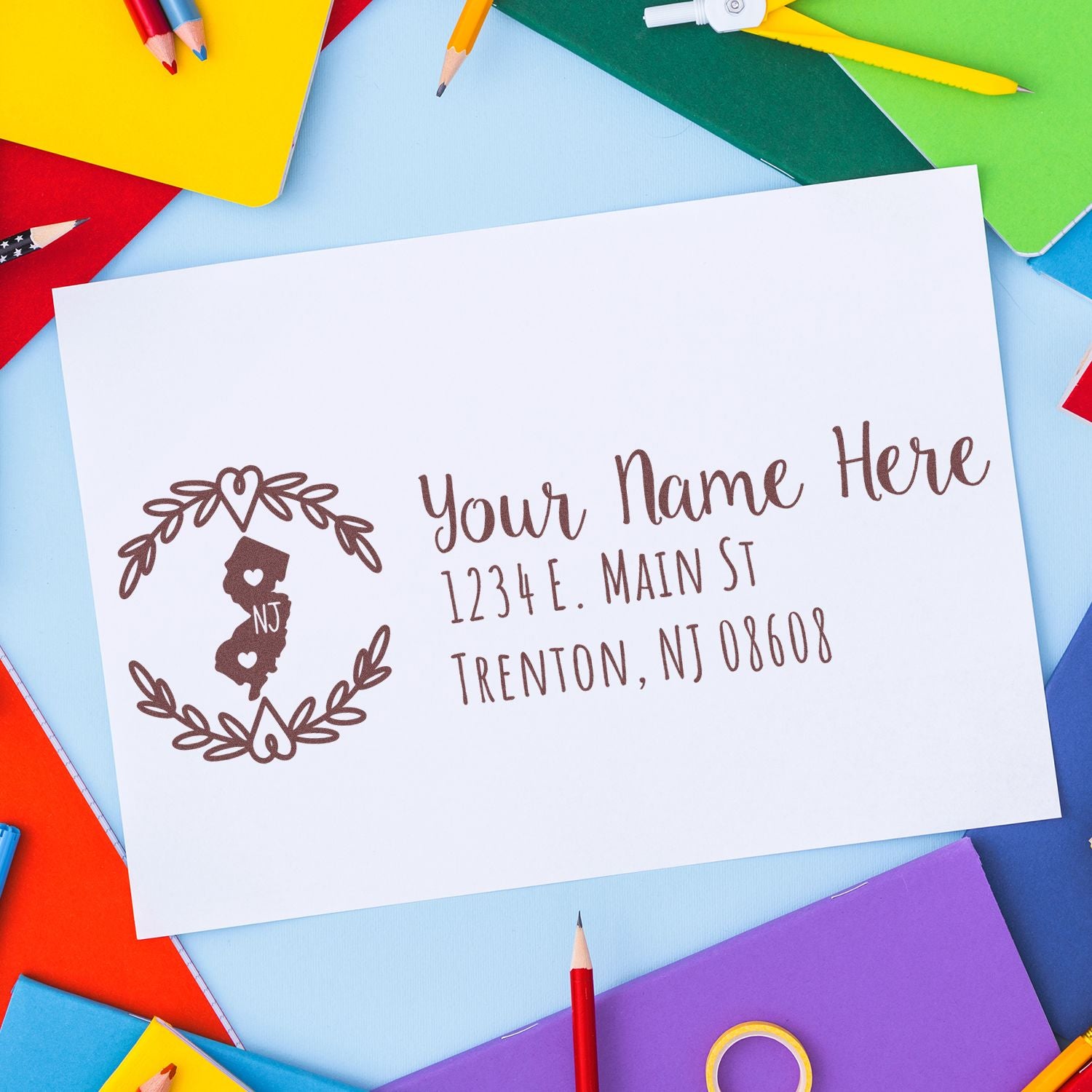 New Jersey State Custom Return Address Stamp on white paper, surrounded by colorful stationery. Features a heart design with NJ and sample address text in elegant script.