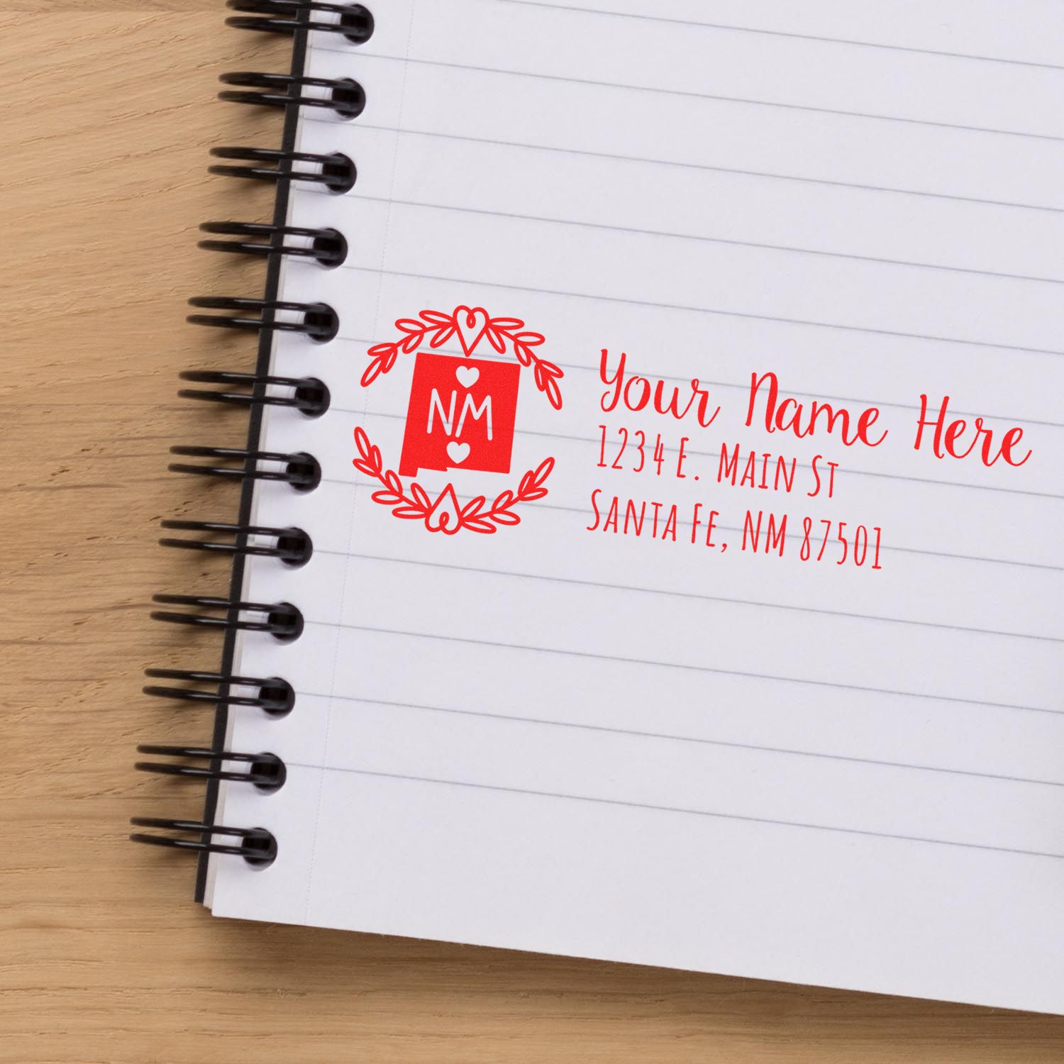 Self-Inking State Wreath of New Mexico Address Stamp in red ink on a notebook, featuring a decorative wreath and customizable address fields.