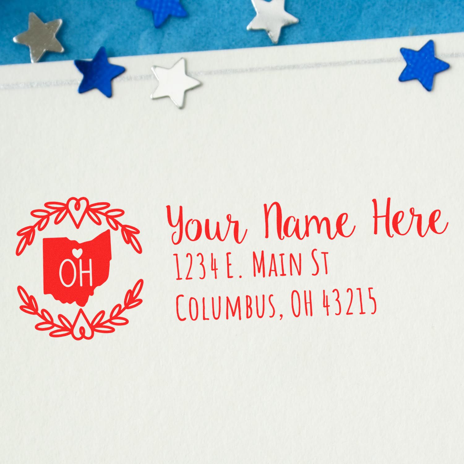 Self-Inking State Wreath of Ohio Address Stamp on an envelope, featuring a red Ohio outline with OH and decorative wreath, surrounded by blue and silver star confetti.