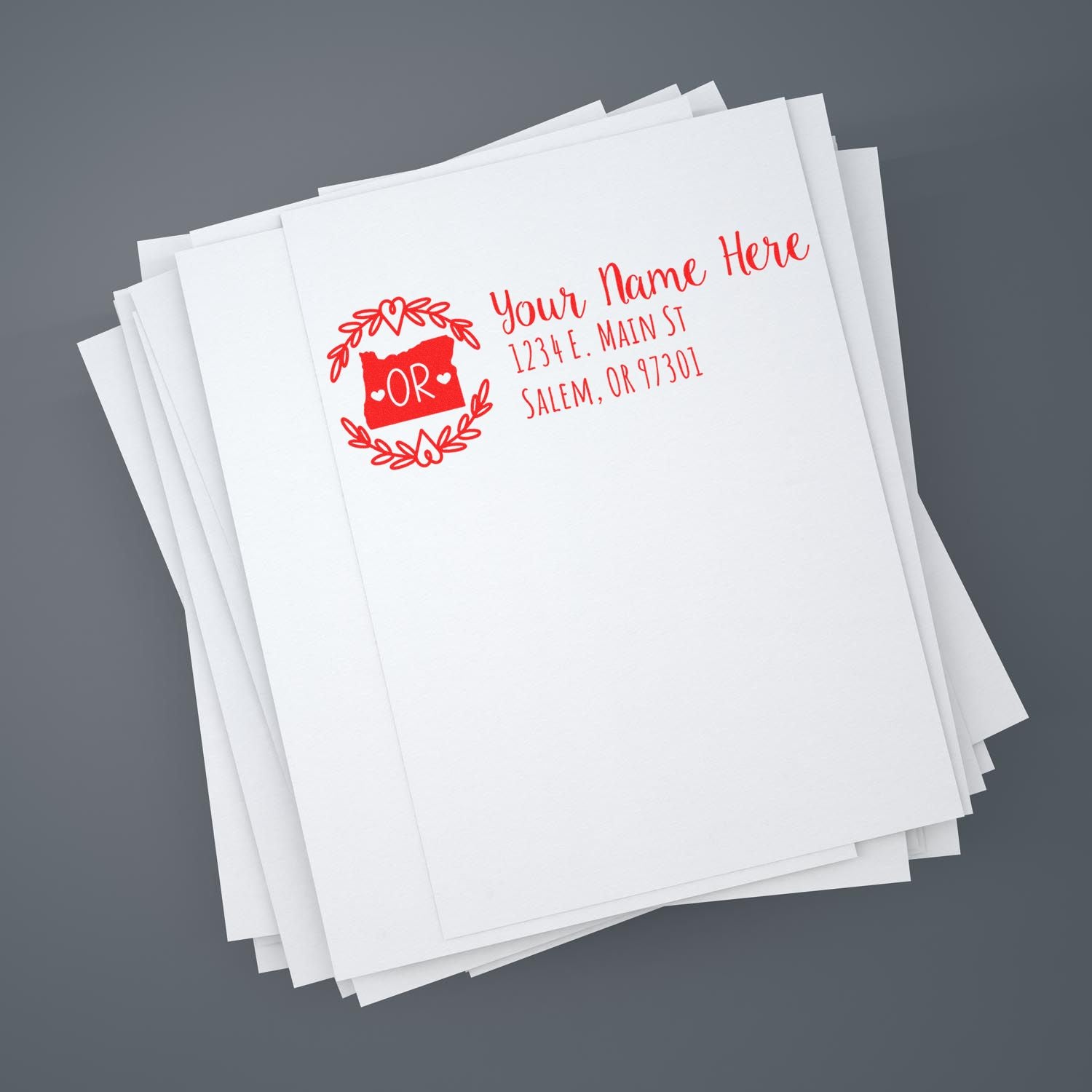 Stack of envelopes featuring the Oregon State Custom Return Address Stamp in red, displaying a personalized name and address with an Oregon state outline and decorative wreath design.