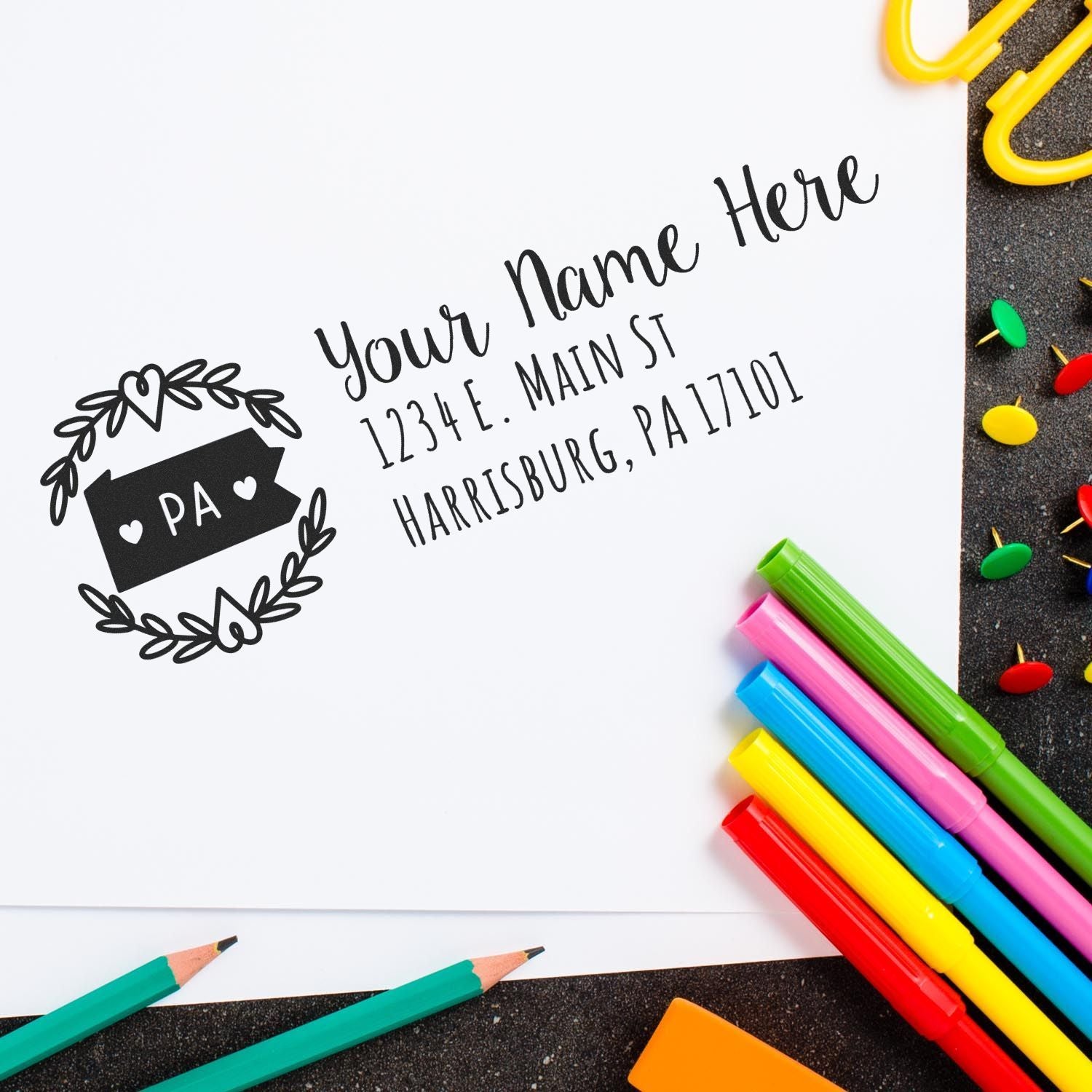 Image of a Pennsylvania State Custom Return Address Stamp on white paper with colorful markers and paperclips. The stamp features a decorative border with PA and space for name and address details.