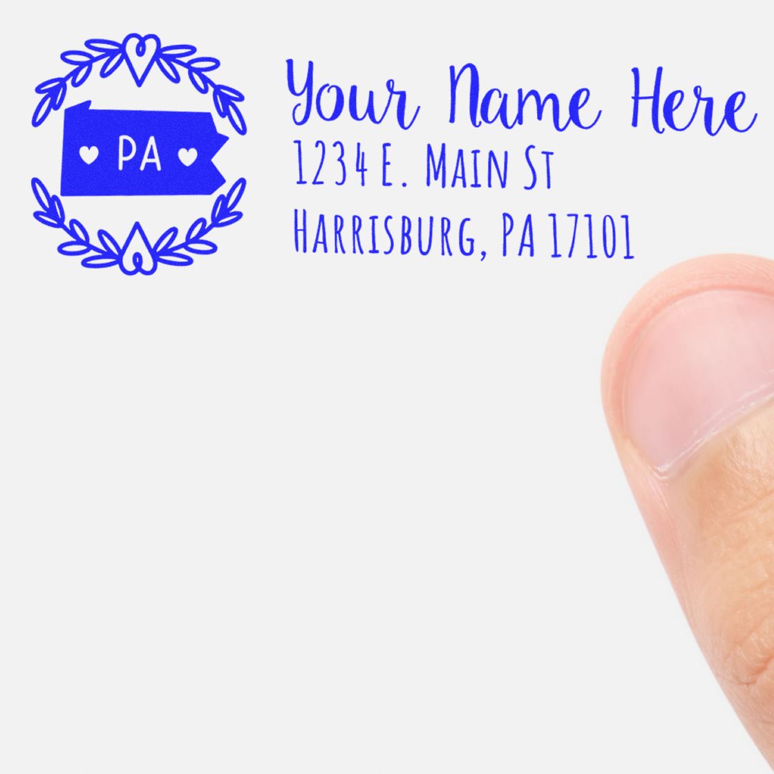 PSI Pre-Inked Pennsylvania State Customized Address Stamp in use, featuring a blue PA state design with placeholder text for name and address, shown next to a person's thumb for scale.