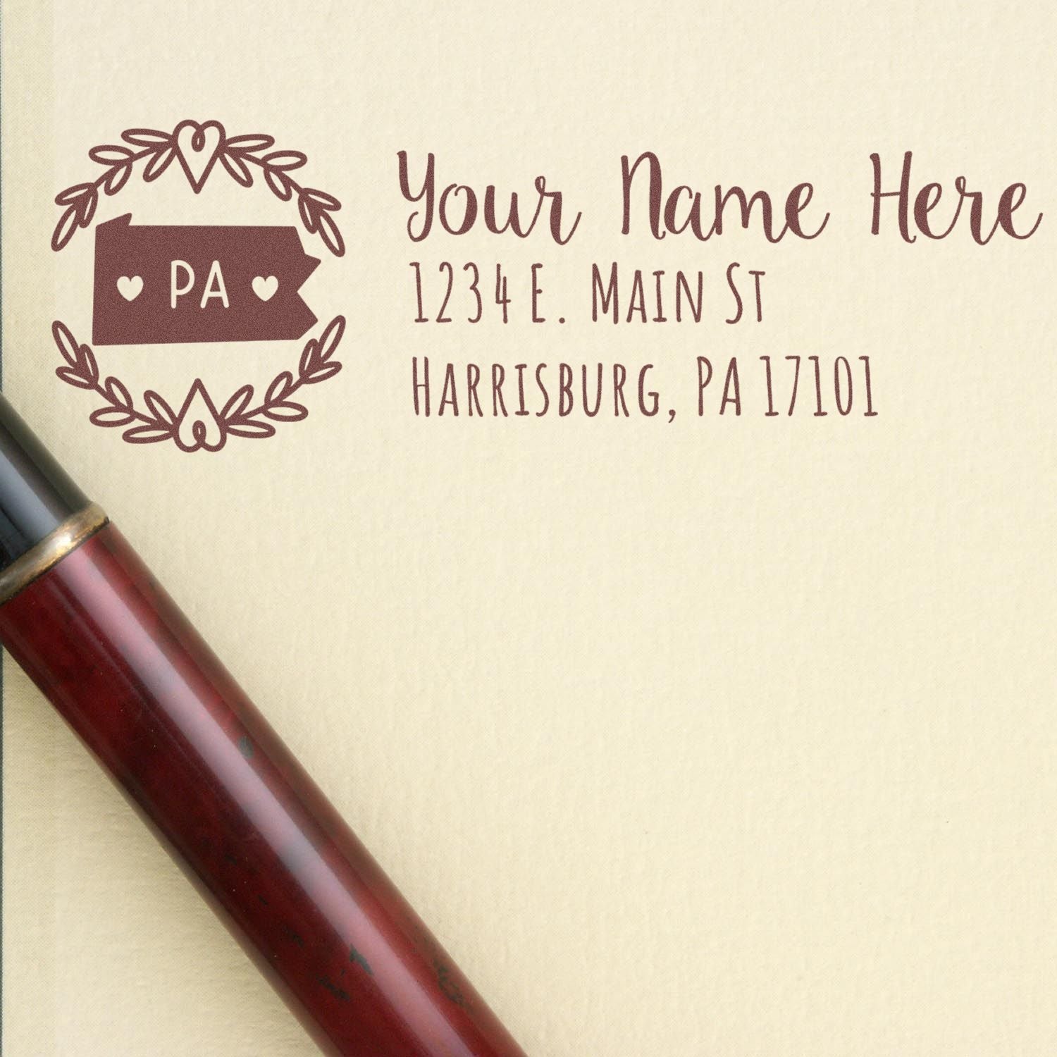 Elegant Pennsylvania State Custom Return Address Stamp on cream paper, featuring a decorative border with 'PA' and space for personalized name and address. A pen lies nearby for added context.