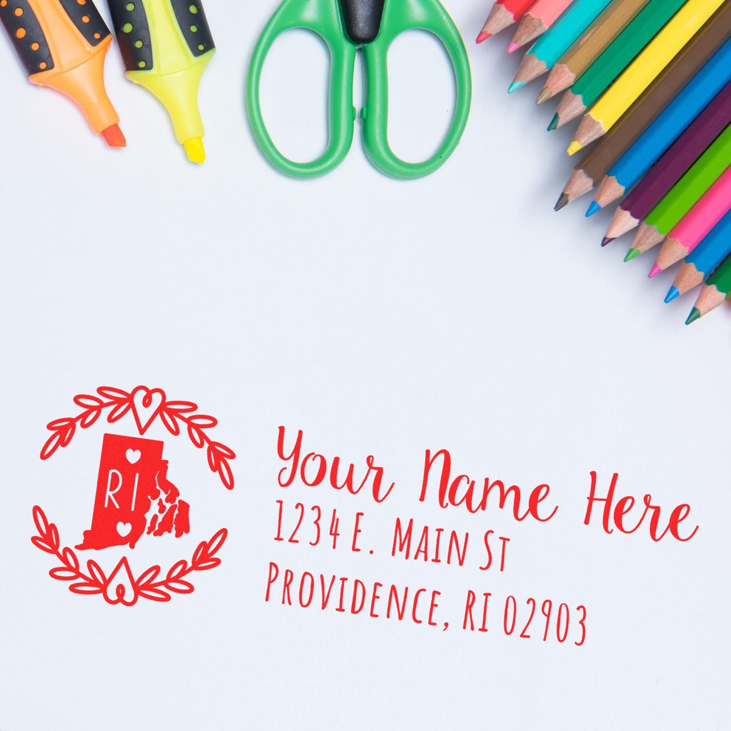 Slim Rhode Island Personalized Pre-Inked Address Stamp in red ink on white paper, surrounded by colorful pencils, scissors, and highlighters. Features a decorative Rhode Island state outline.