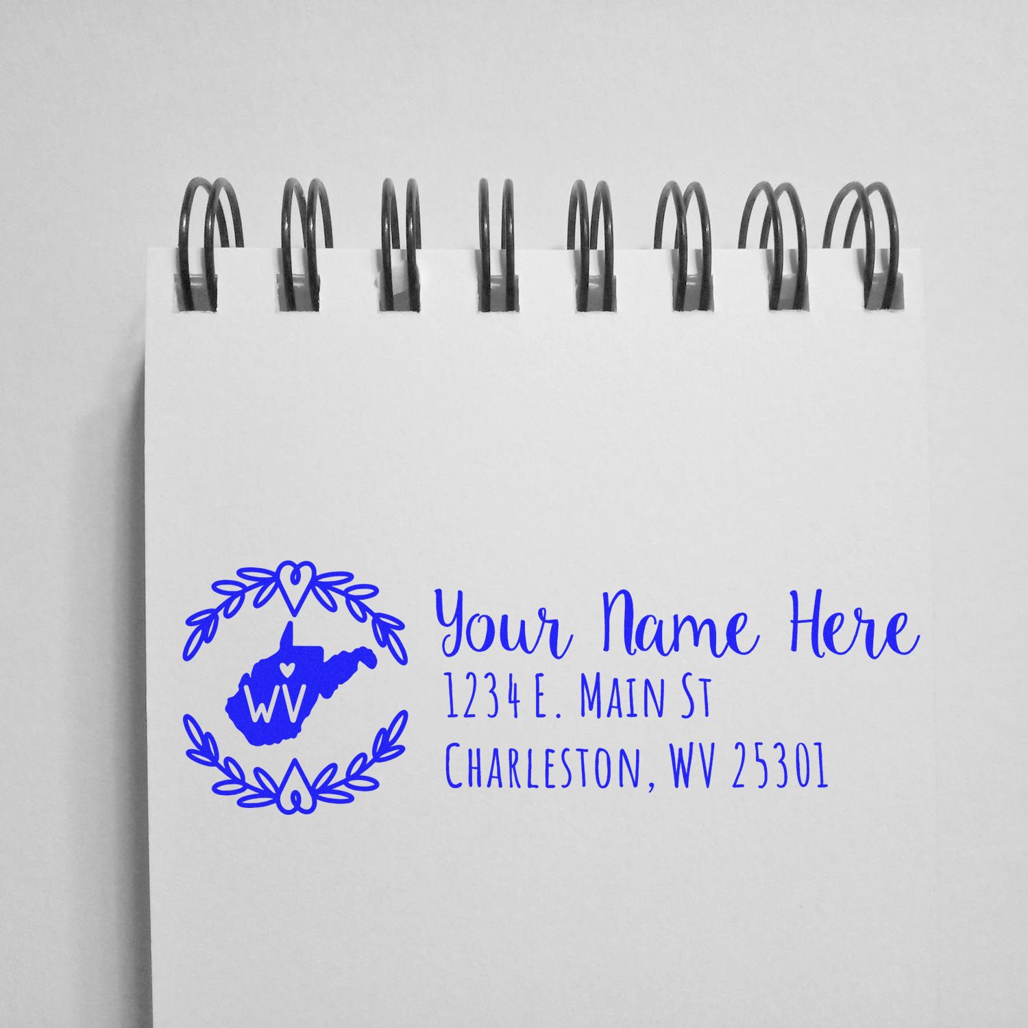 Self-Inking State Wreath of West Virginia Address Stamp on notepad, featuring a blue state outline with heart and wreath design, customizable address and name in elegant font.