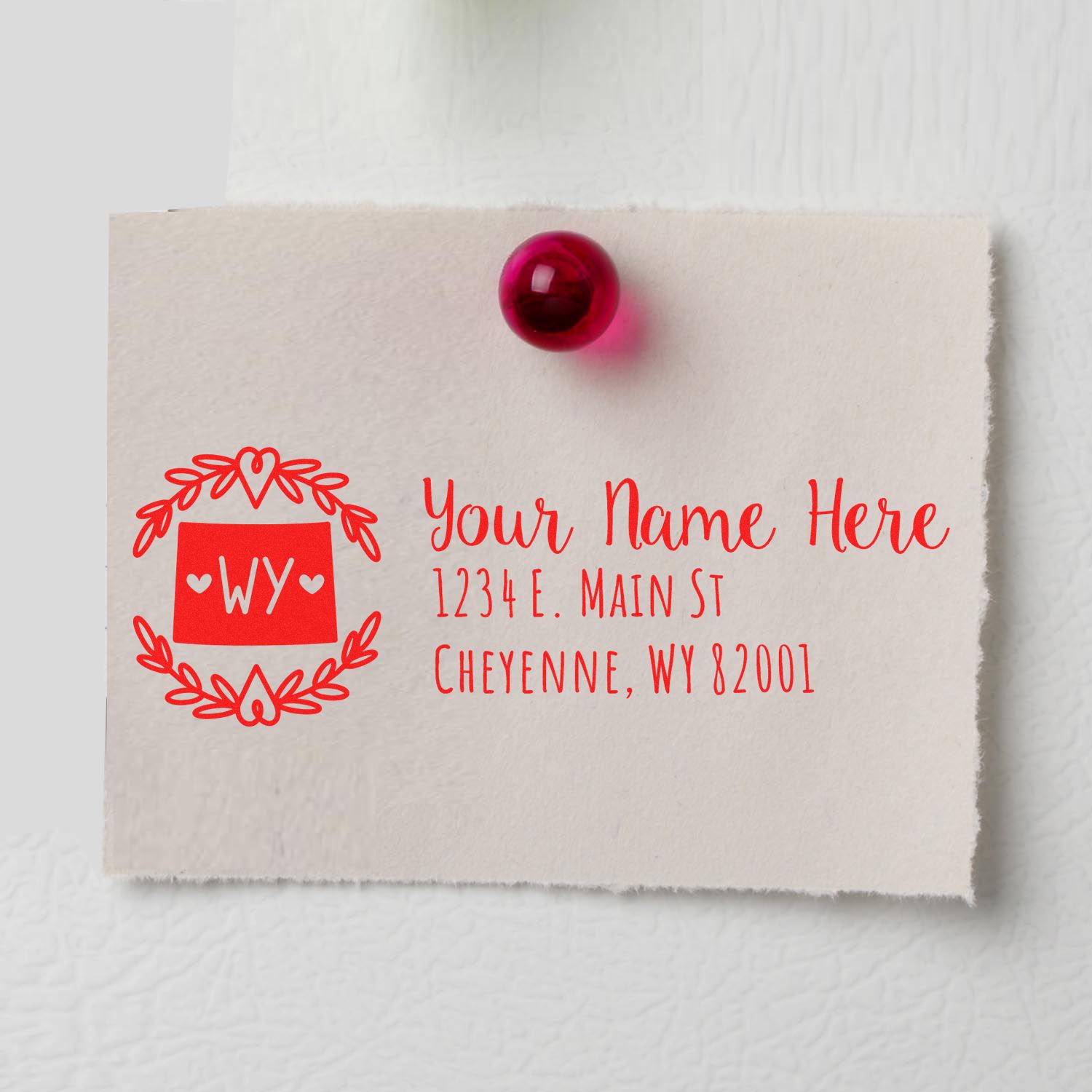 Wyoming State Custom Return Address Stamp on a beige card with red ink, featuring a decorative border and placeholder text for name and address, pinned to a surface with a red pushpin.