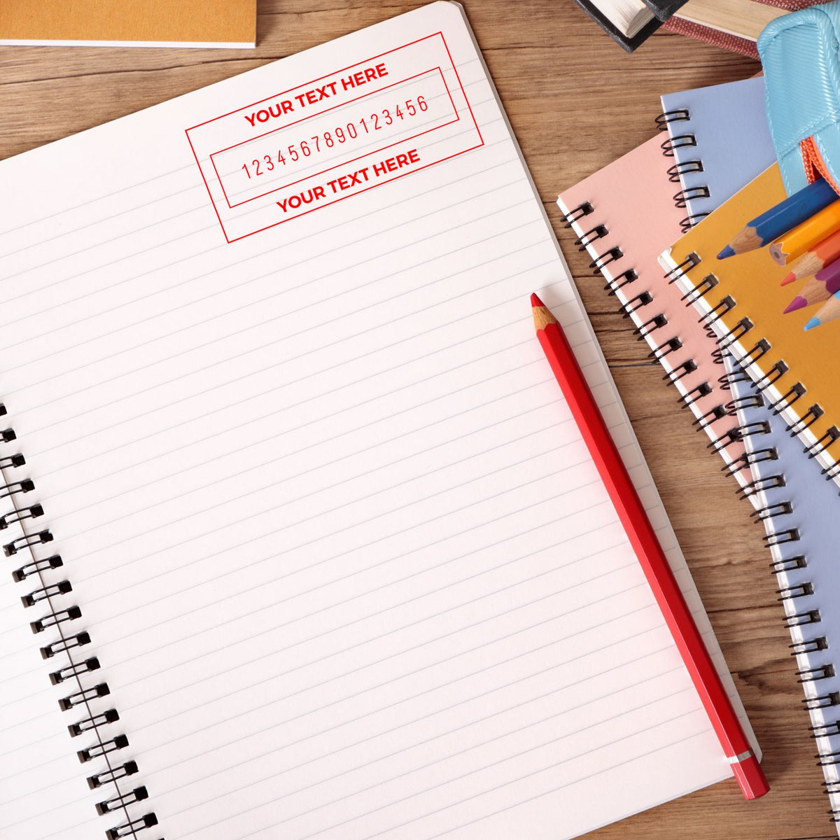 Blank lined notebook with red custom stamp seal impression, red pencil, and colorful spiral notebooks on a wood desk