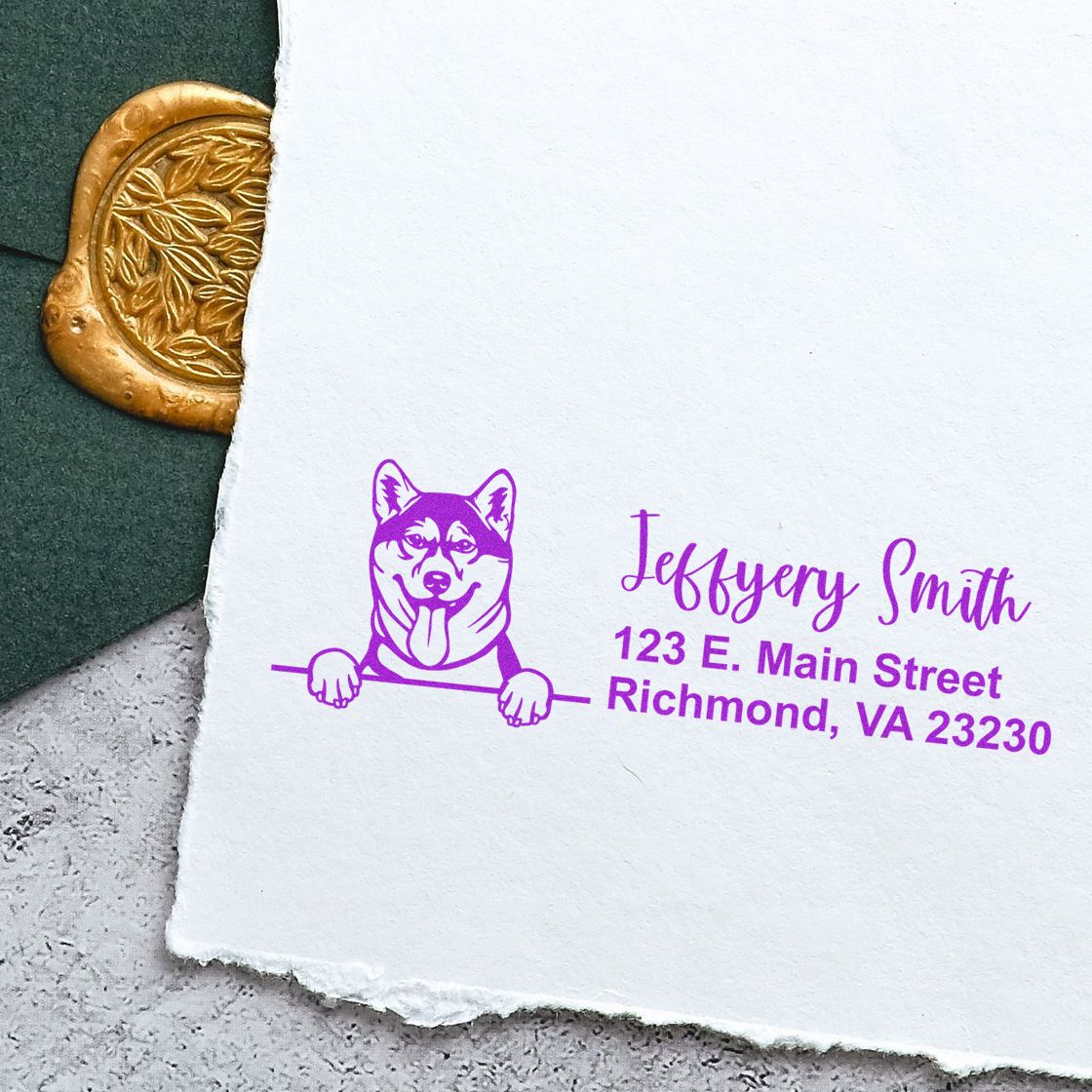 Purple custom stamp with dog logo and address on white paper, beside a gold wax seal on green fabric.
