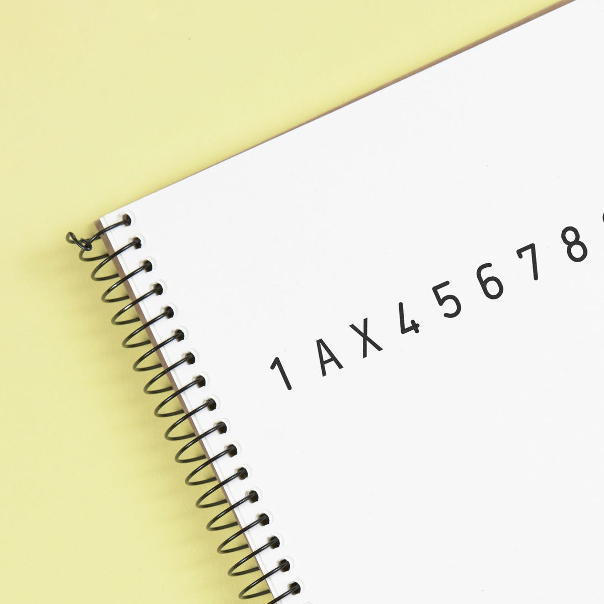 White spiral notebook on pale yellow background with black alphanumeric stamp and seal code 1AX45678.