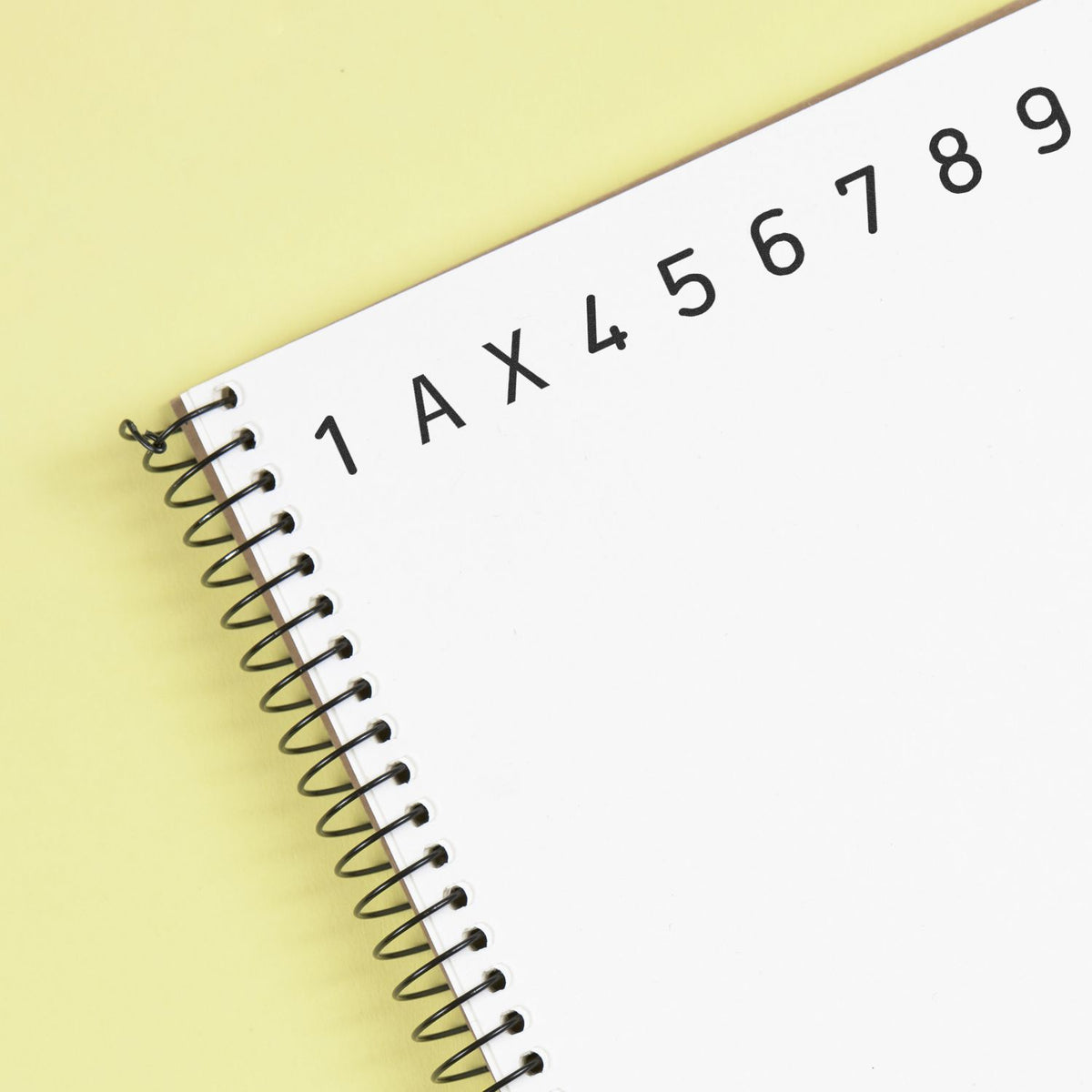 White spiral-bound stamp and seal product with black 1AX456789 print on a pale yellow background.