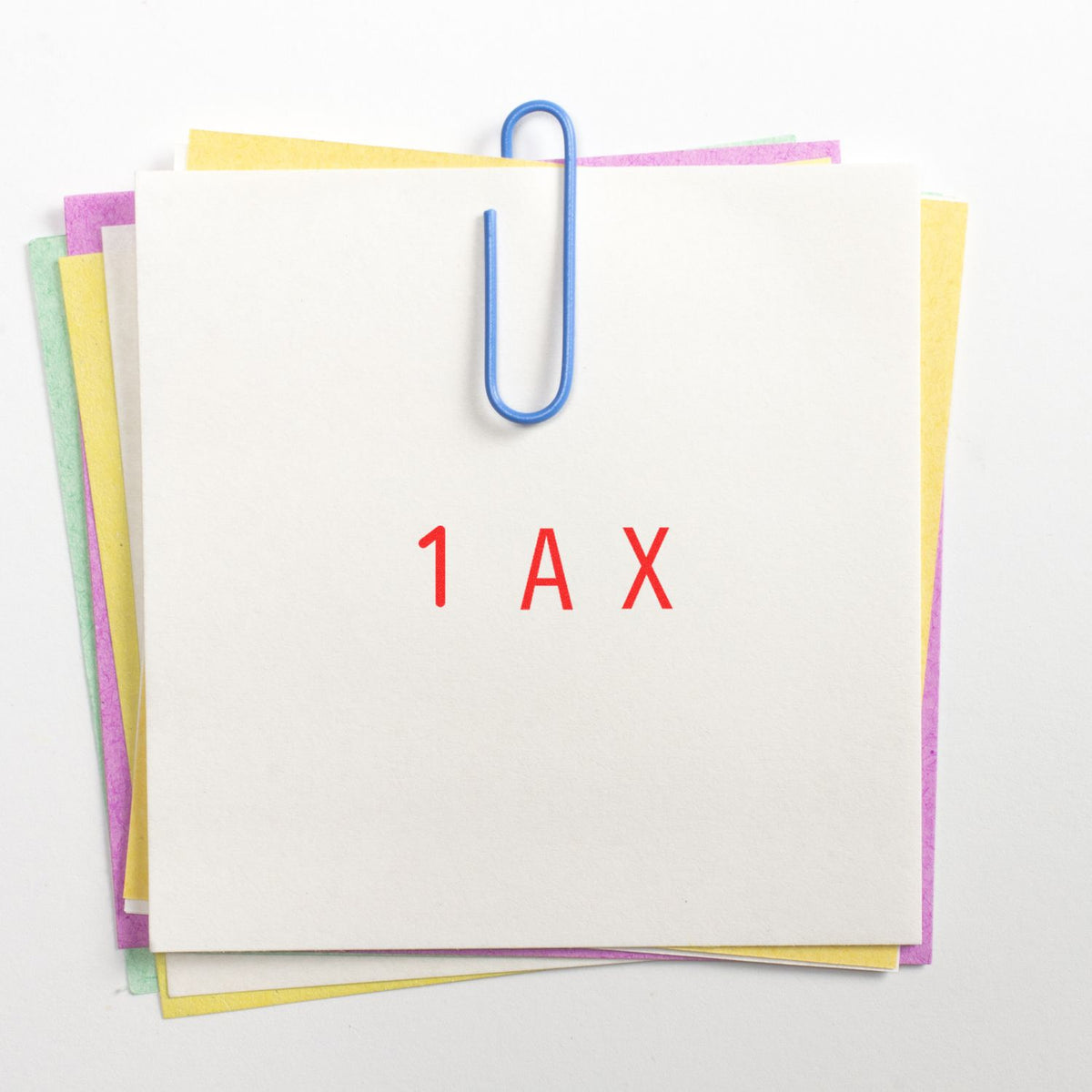 Stacked pastel paper sheets clipped with a blue paperclip and red 1AX stamp, seal, and marking supply.