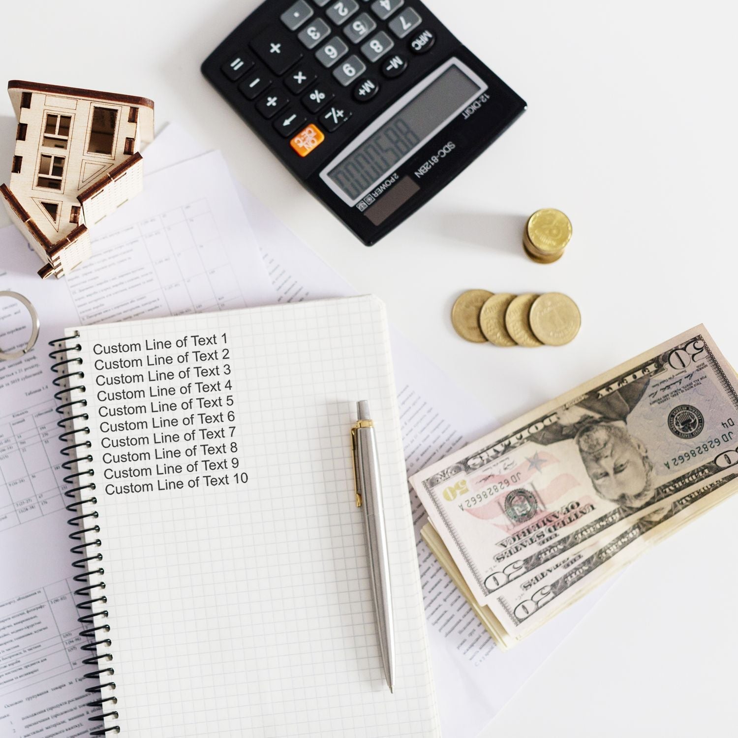 A 10 Line Custom Rubber Stamp with Wood Handle is shown stamping a notebook. Nearby are a calculator, coins, cash, and house model.