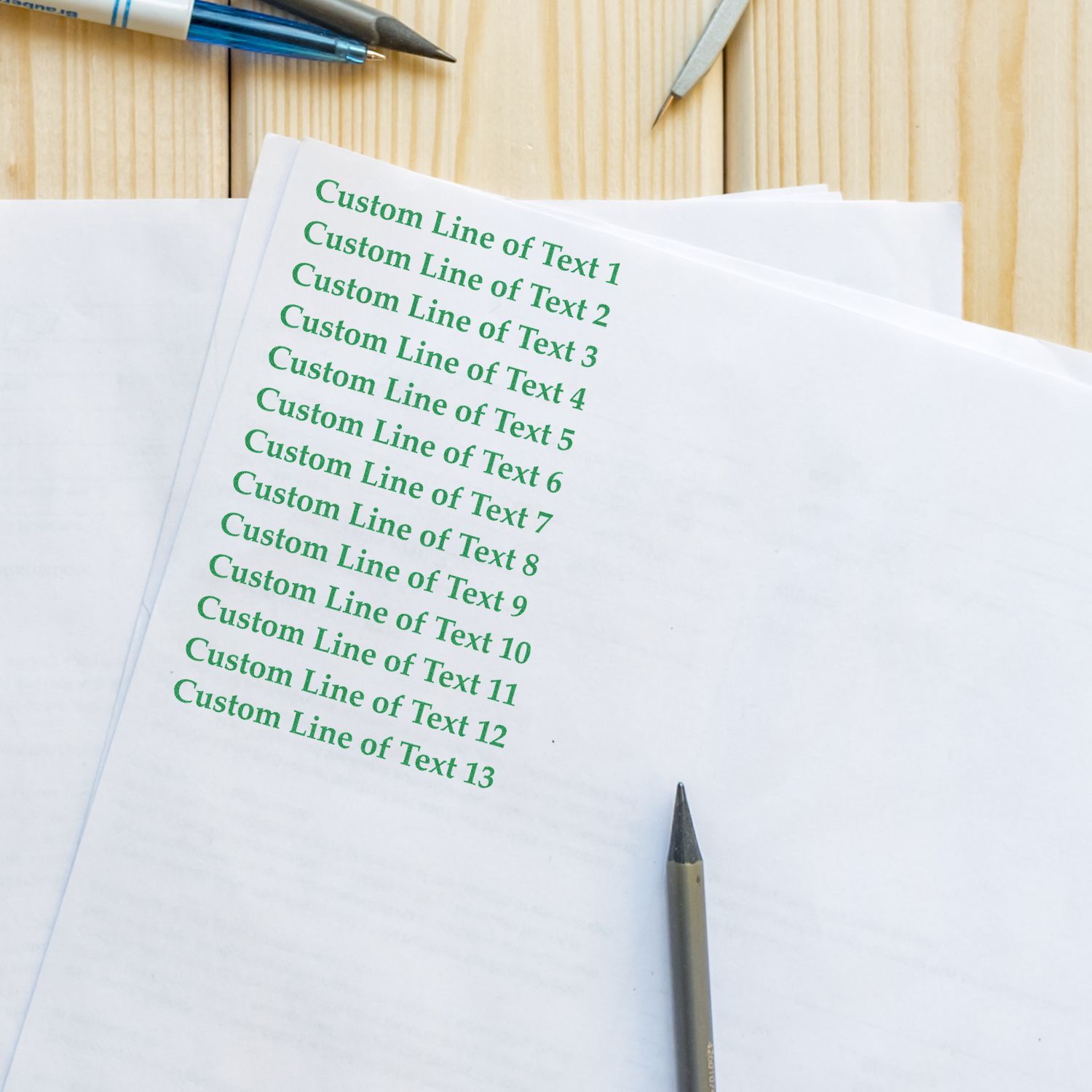 13 Line Custom Rubber Stamp with Wood Handle in use, stamping green text on white paper, surrounded by pens and a pencil on a wooden surface.