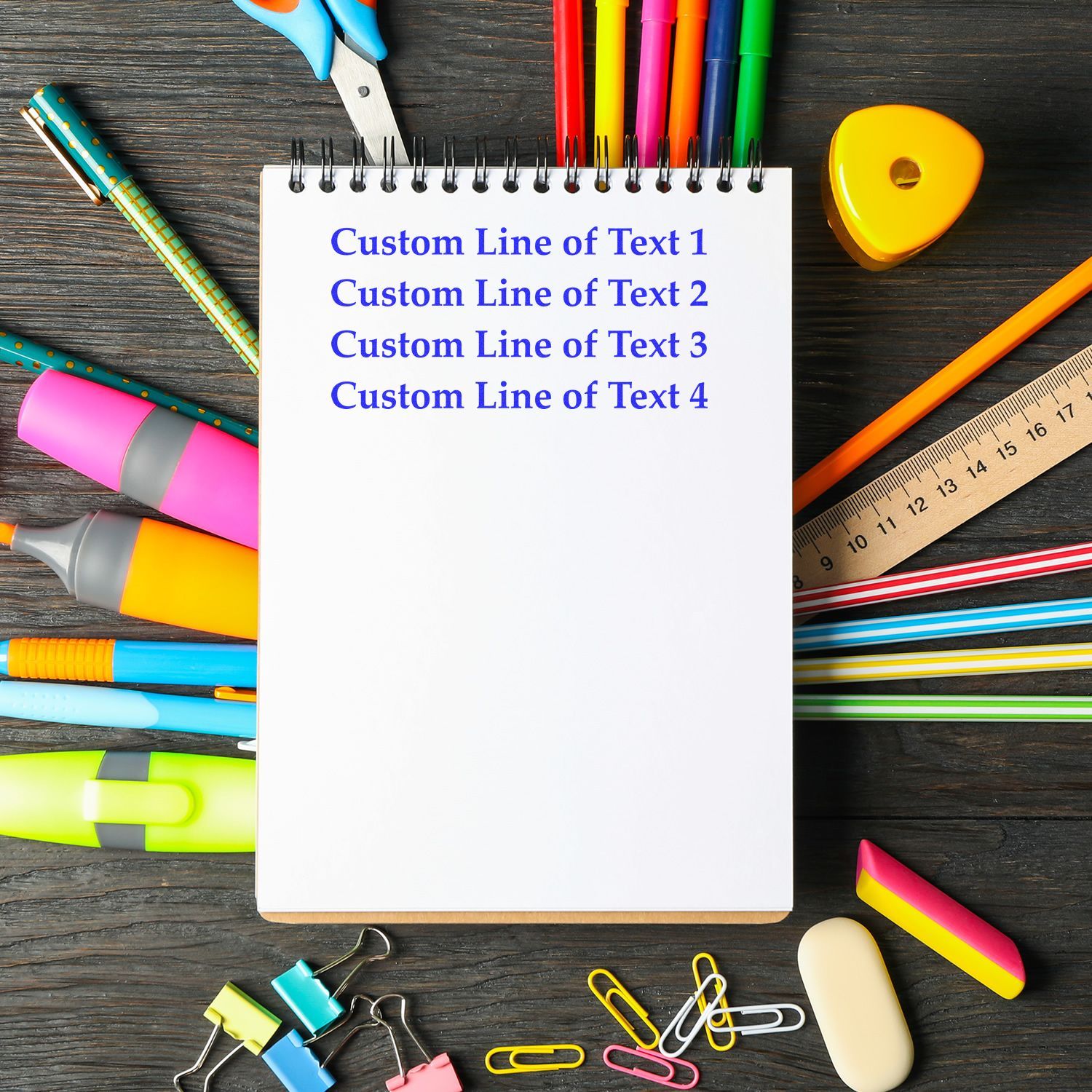 A 4 Line Custom Rubber Stamp with Wood Handle is shown stamping a notebook surrounded by colorful stationery on a wooden desk.