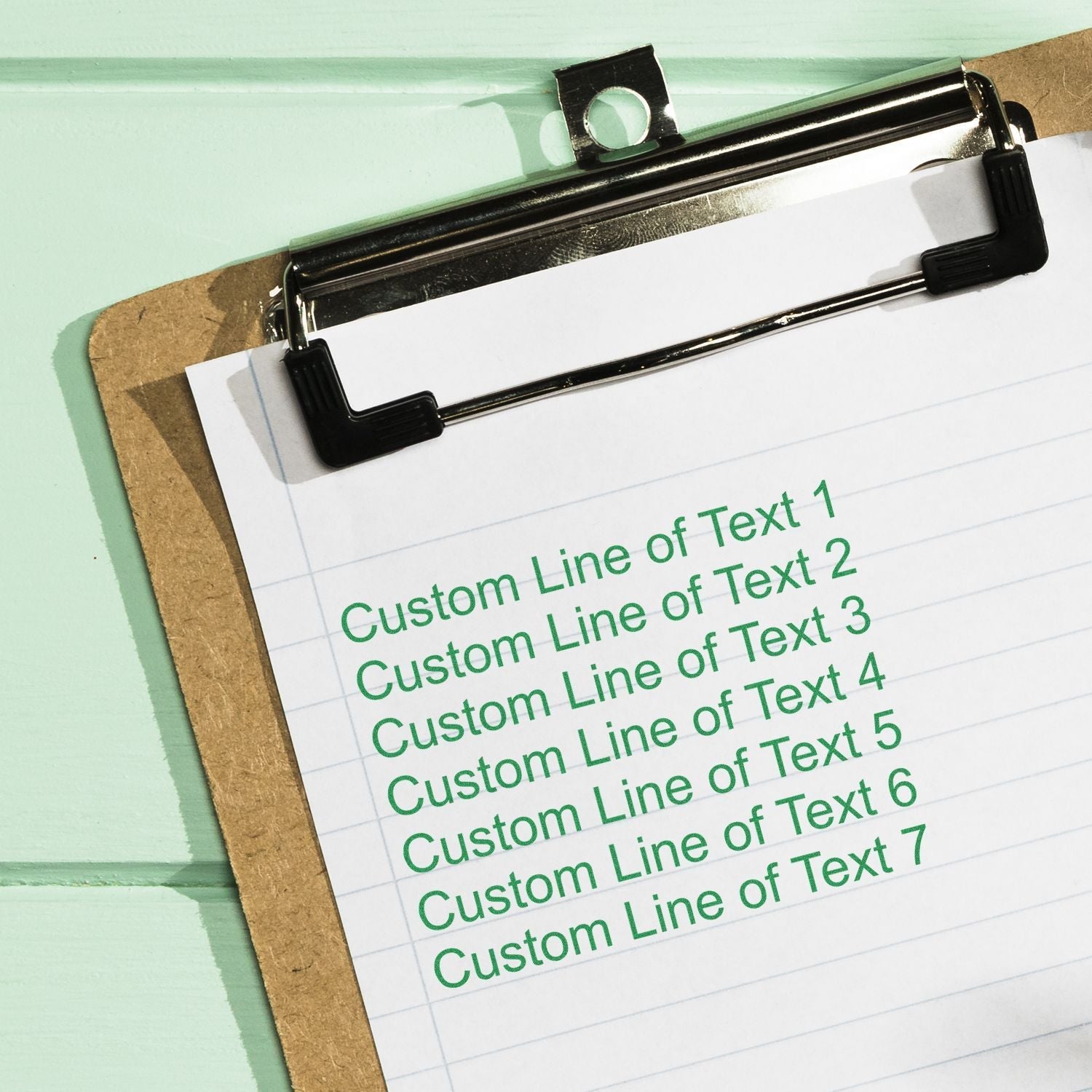 A 7 Line Custom Rubber Stamp with Wood Handle is used to stamp green text on a clipboard with lined paper.