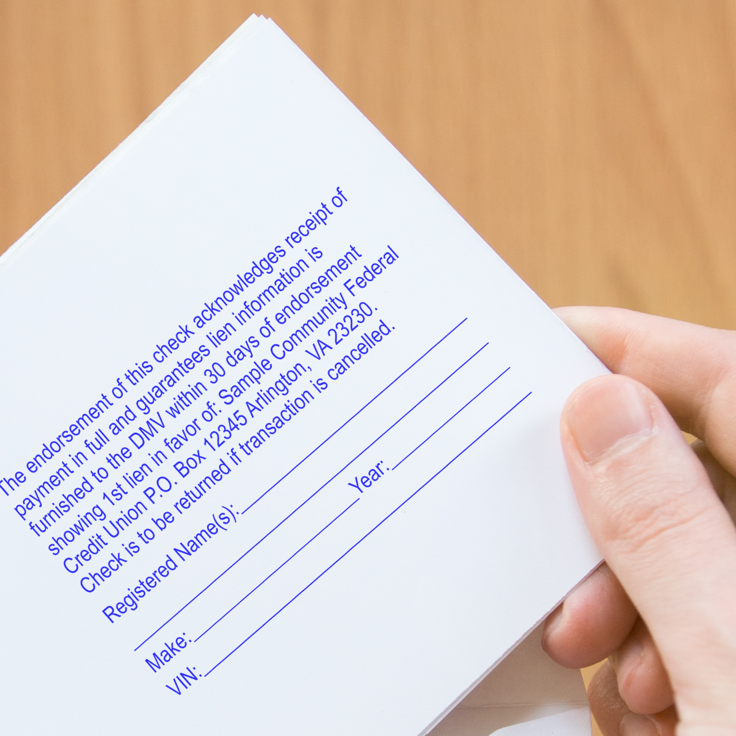 A hand holding a document stamped with blue ink using a 10 Line Custom Rubber Stamp with Wood Handle, showing lines for name, date, and VIN.