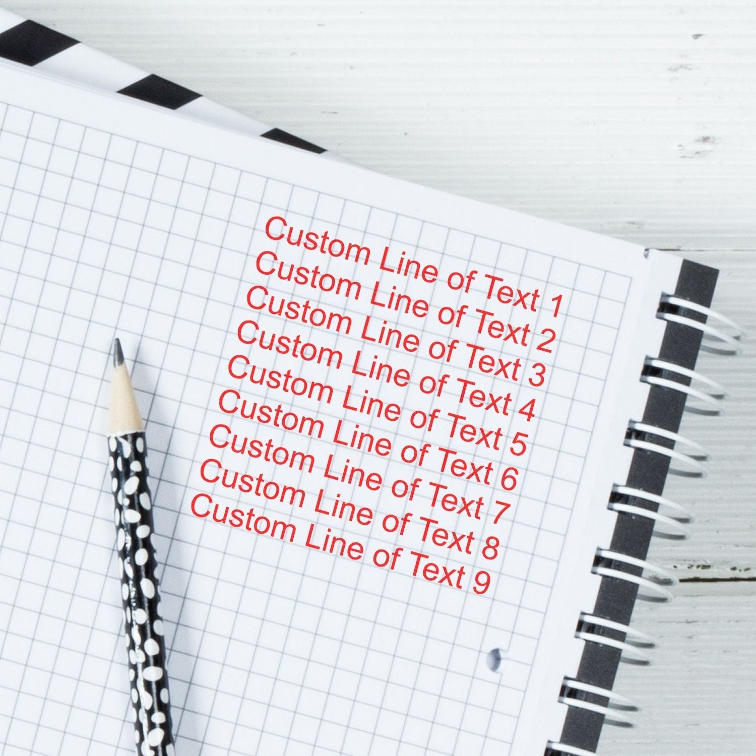 9 Line Custom Rubber Stamp with Wood Handle used on a notebook, displaying nine lines of red text. A pencil lies beside the notebook.