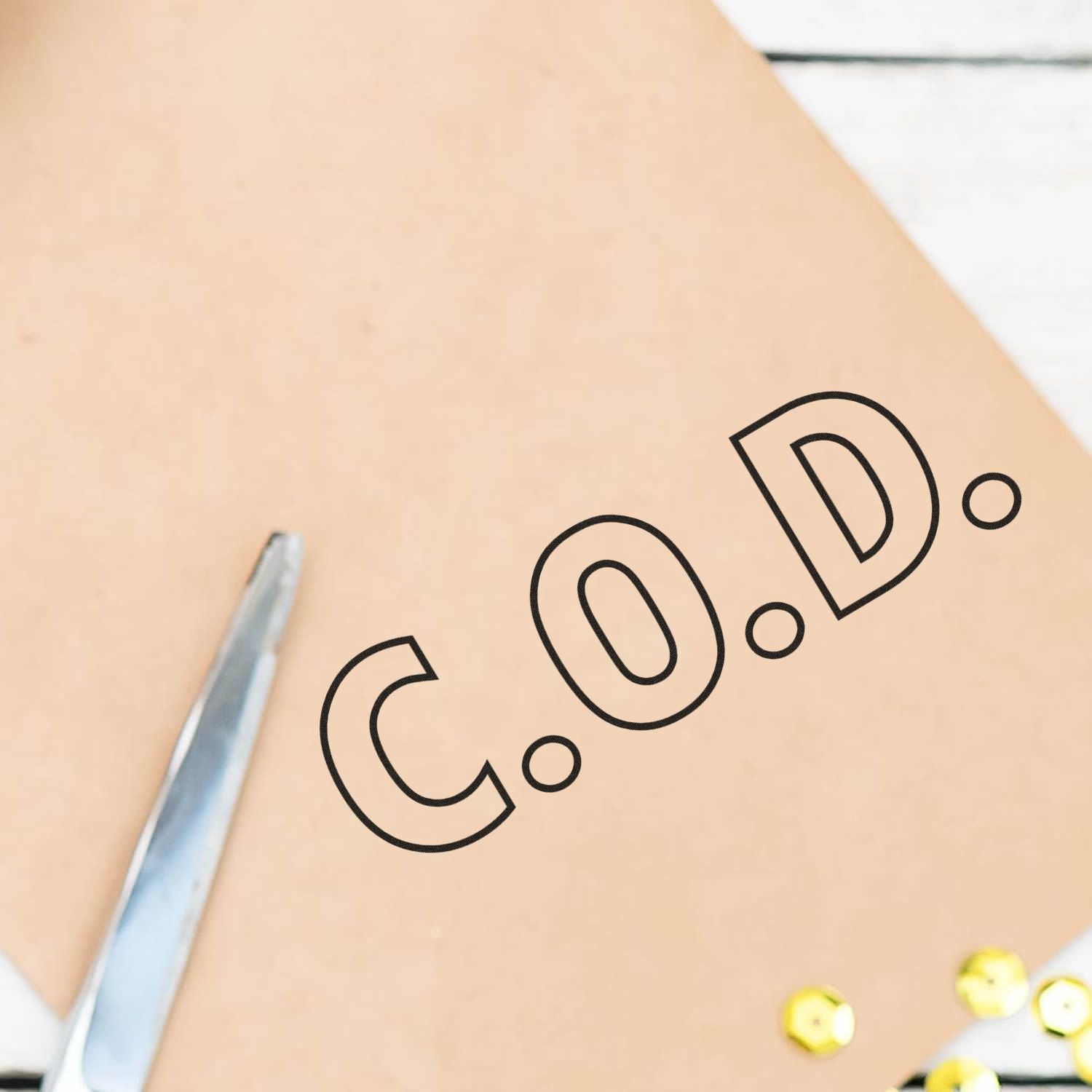 Large Pre-Inked C.O.D. Outline Stamp on brown paper with scissors and yellow sequins nearby.