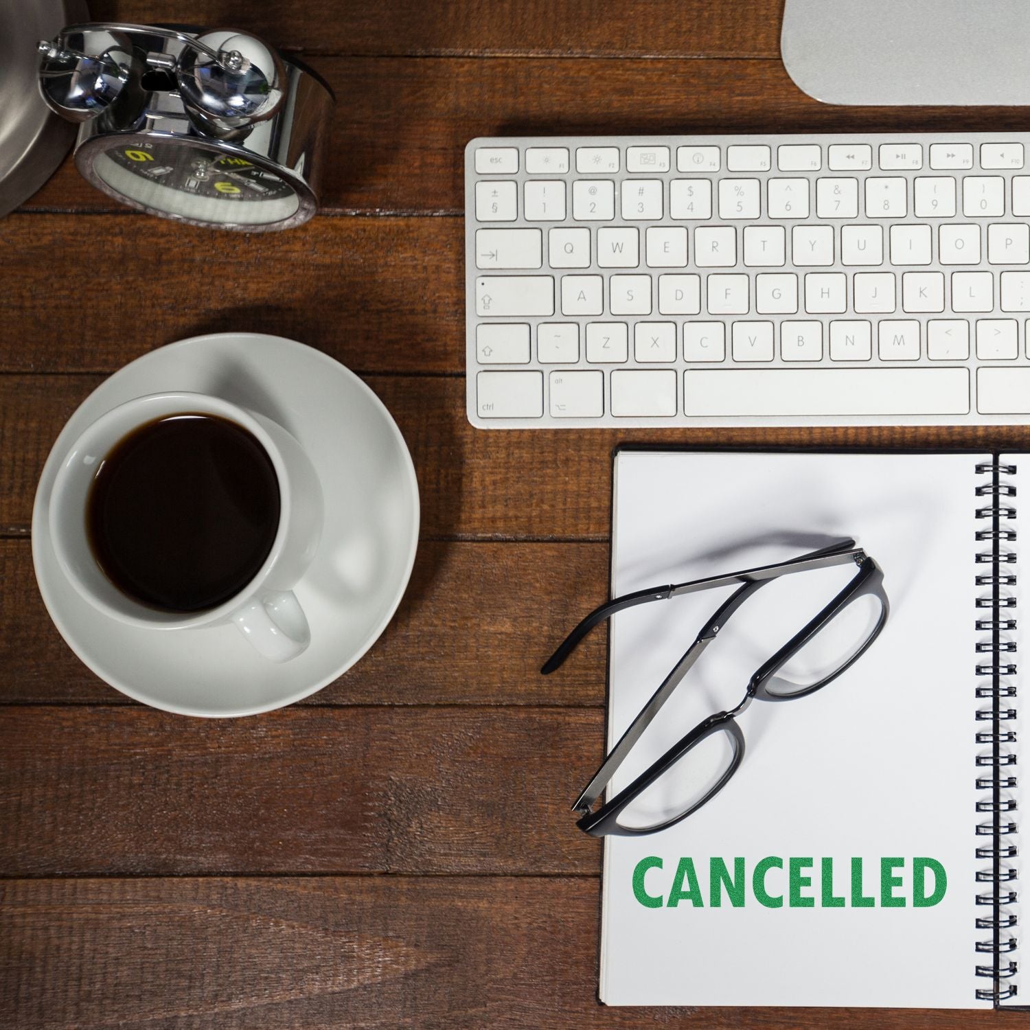 A desk with a keyboard, coffee, glasses, and a notebook stamped with CANCELLED using a Large Pre-Inked Cancelled Stamp.