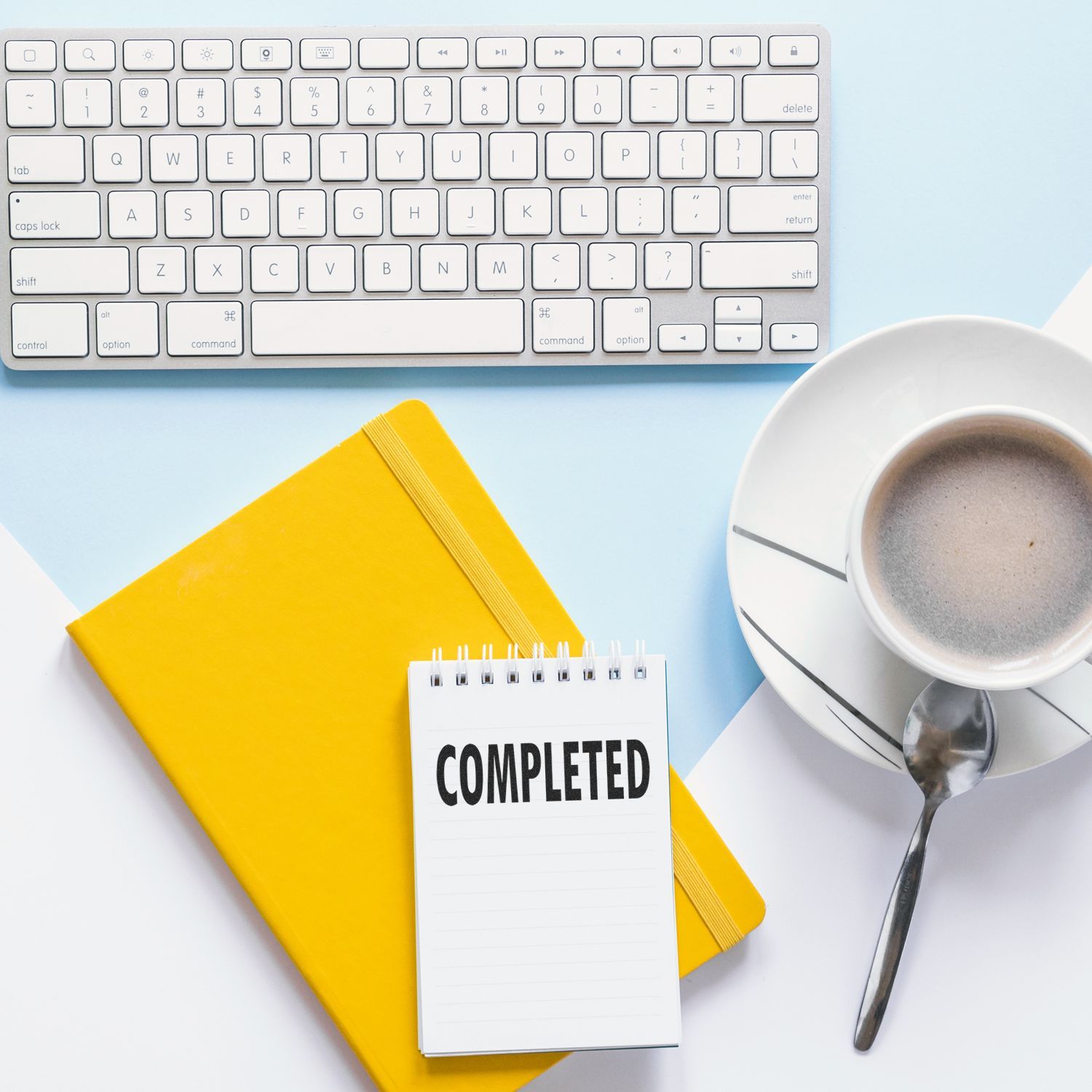 A Large Pre-Inked Completed Stamp on a notepad, next to a yellow notebook, a keyboard, and a cup of coffee on a light blue and white background.