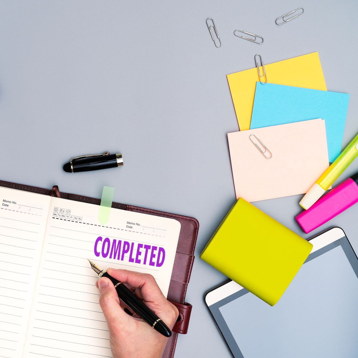 Person using a Large Pre-Inked Completed Stamp on a planner, surrounded by colorful sticky notes, paper clips, a pen, and a tablet.