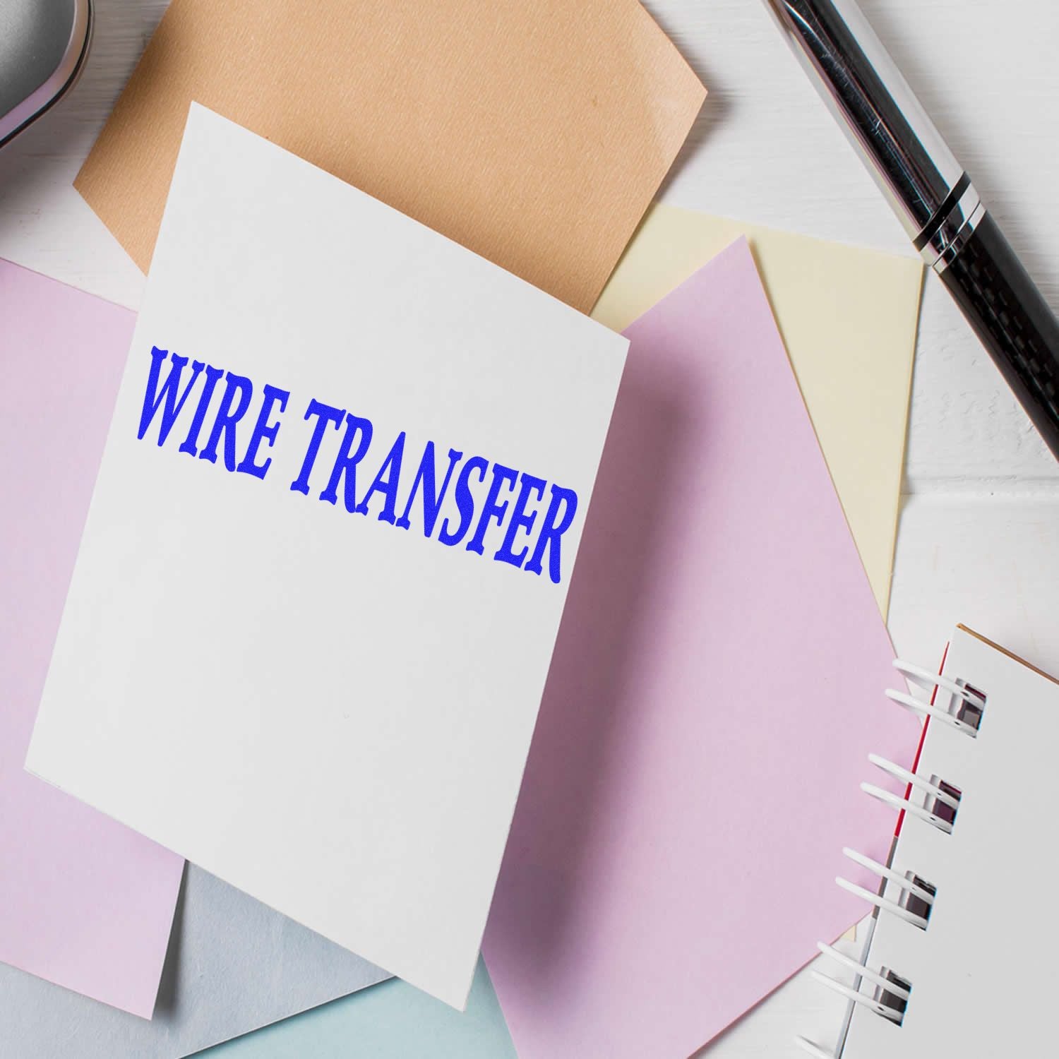 Large Pre-Inked Wire Transfer Stamp on a white card surrounded by pastel-colored papers, a pen, and a notebook.