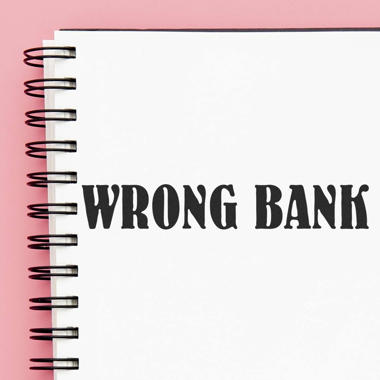 Large Pre-Inked Wrong Bank Stamp imprint on a white spiral notebook page with a pink background.