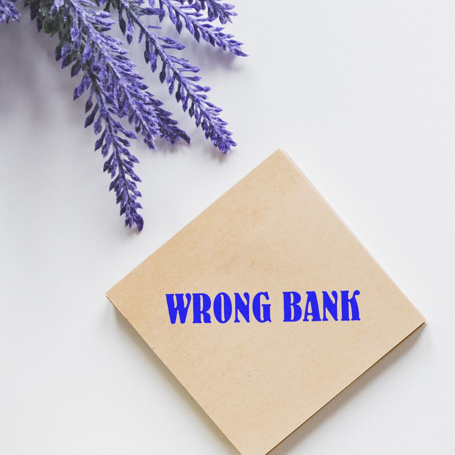 Large Pre-Inked Wrong Bank Stamp on a brown square pad, placed on a white surface with purple lavender flowers in the corner.