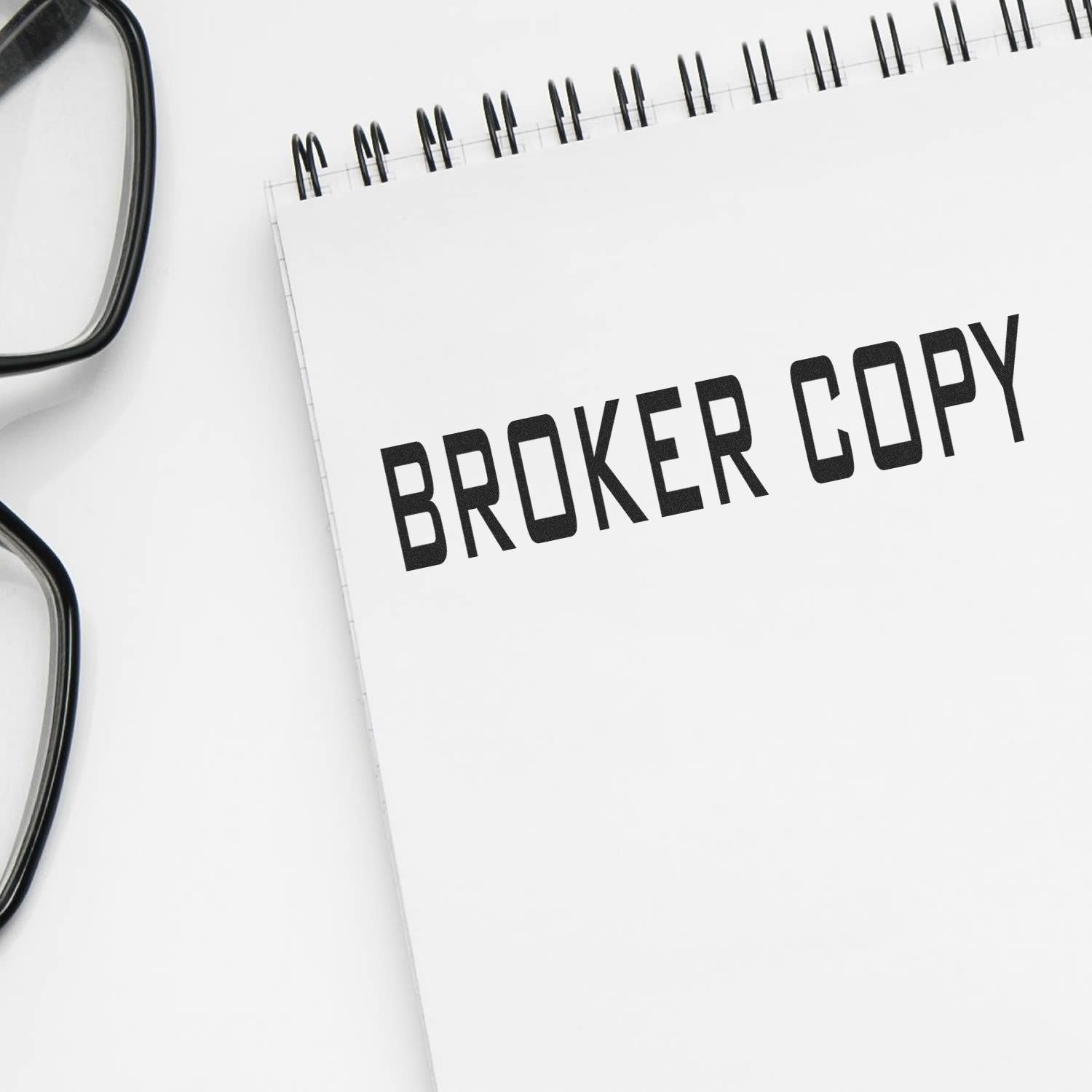 A notebook stamped with BROKER COPY using the Large Pre-Inked Broker Copy Stamp, placed next to a pair of black-framed glasses.