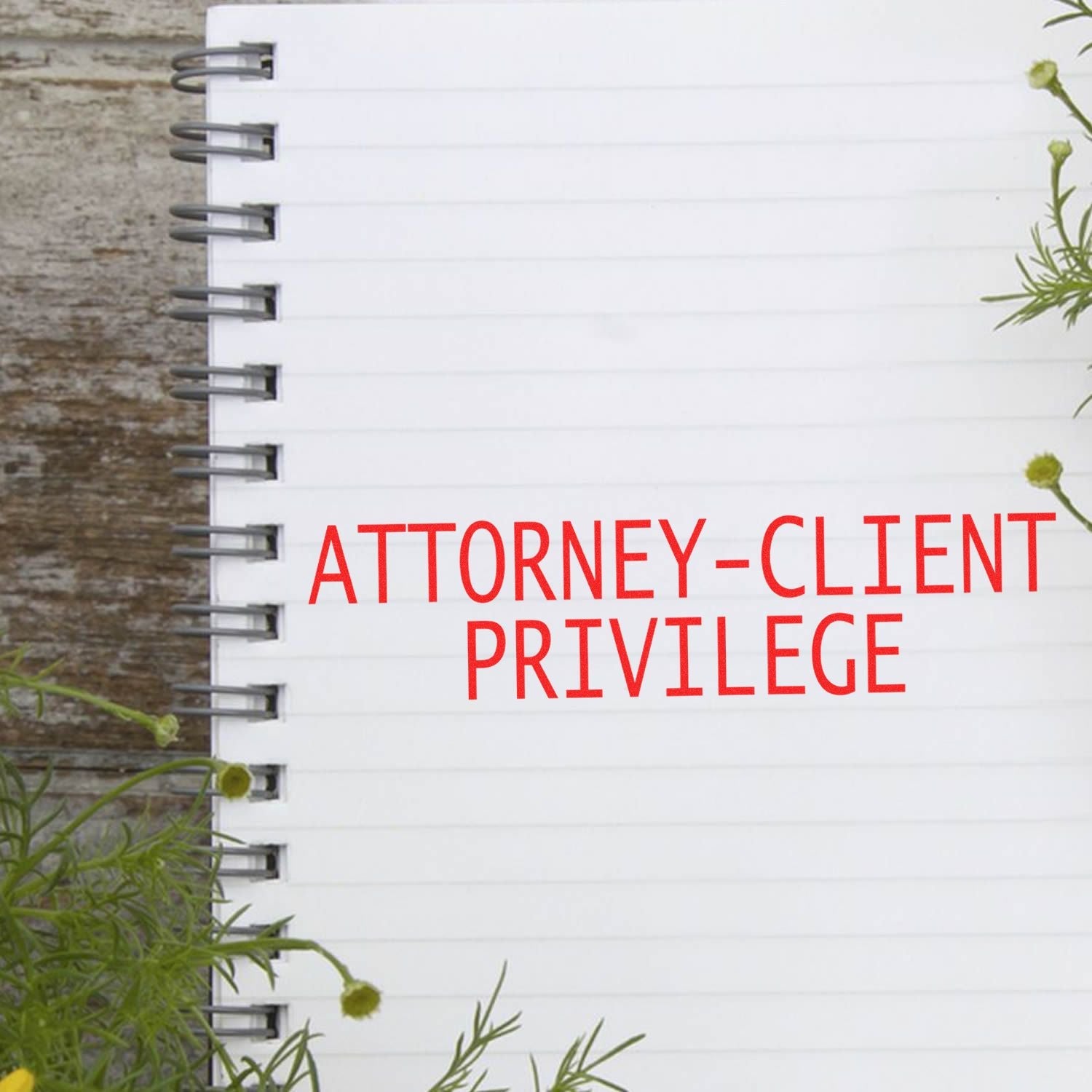 Large Pre Inked Attorney Client Privilege Stamp in red ink on a white spiral notebook, surrounded by green plants.