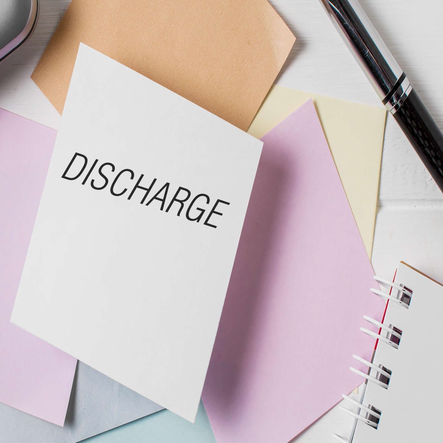 Large Pre-Inked Discharge Stamp on a white card surrounded by pastel-colored papers, a pen, and a spiral notebook.