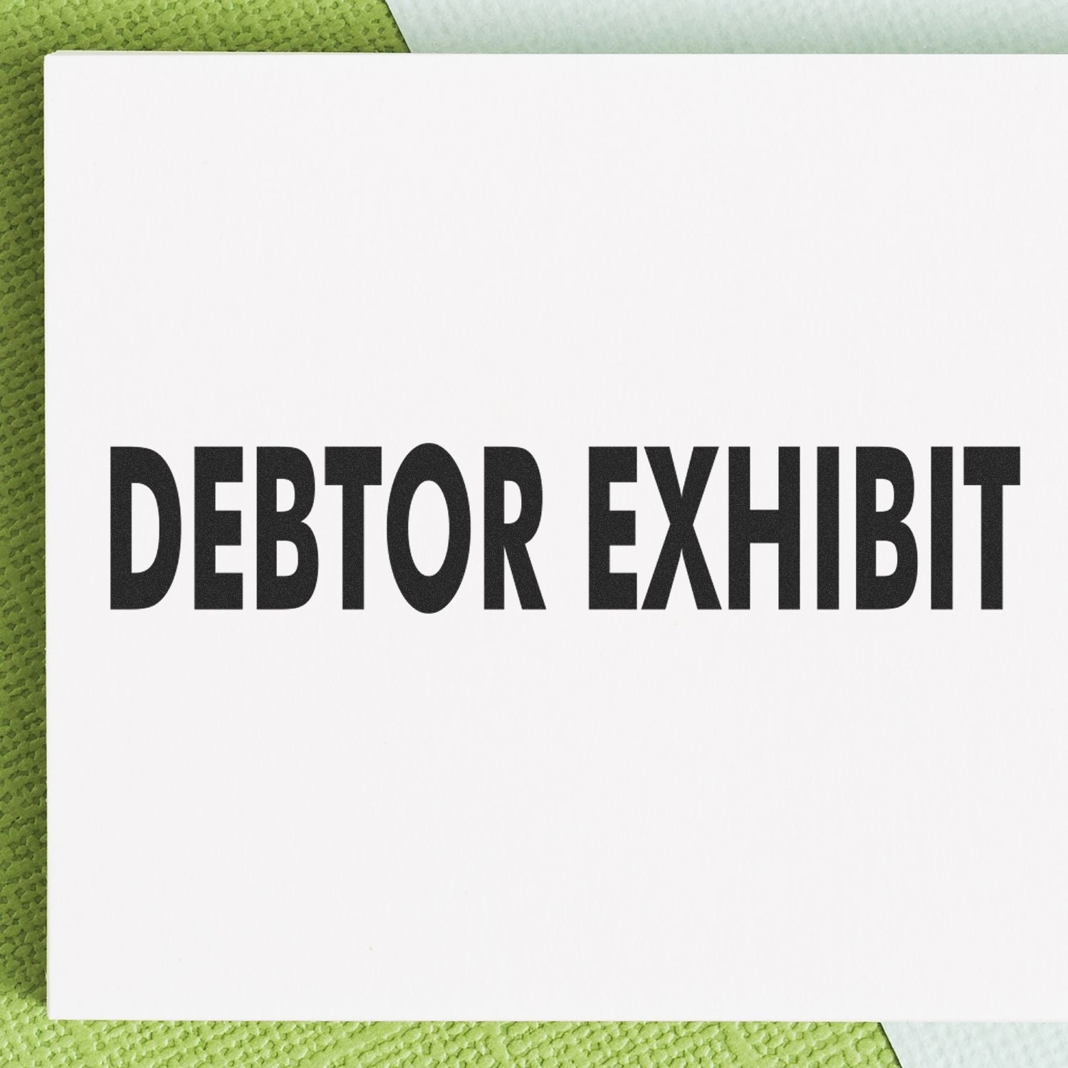 Large Pre-Inked Debtor Exhibit Stamp with bold black text on a white background, placed on a textured green and white surface.