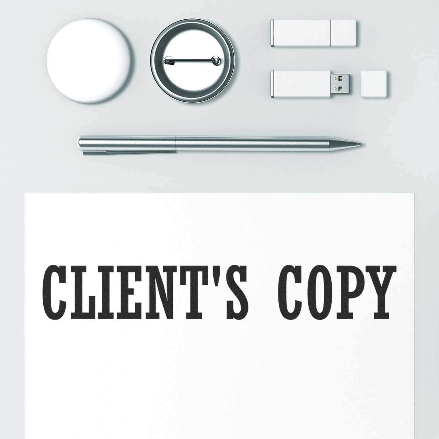 Large Pre-Inked Clients Copy Stamp on a white paper, surrounded by a pen, USB drives, a round badge, and a circular object on a white surface.