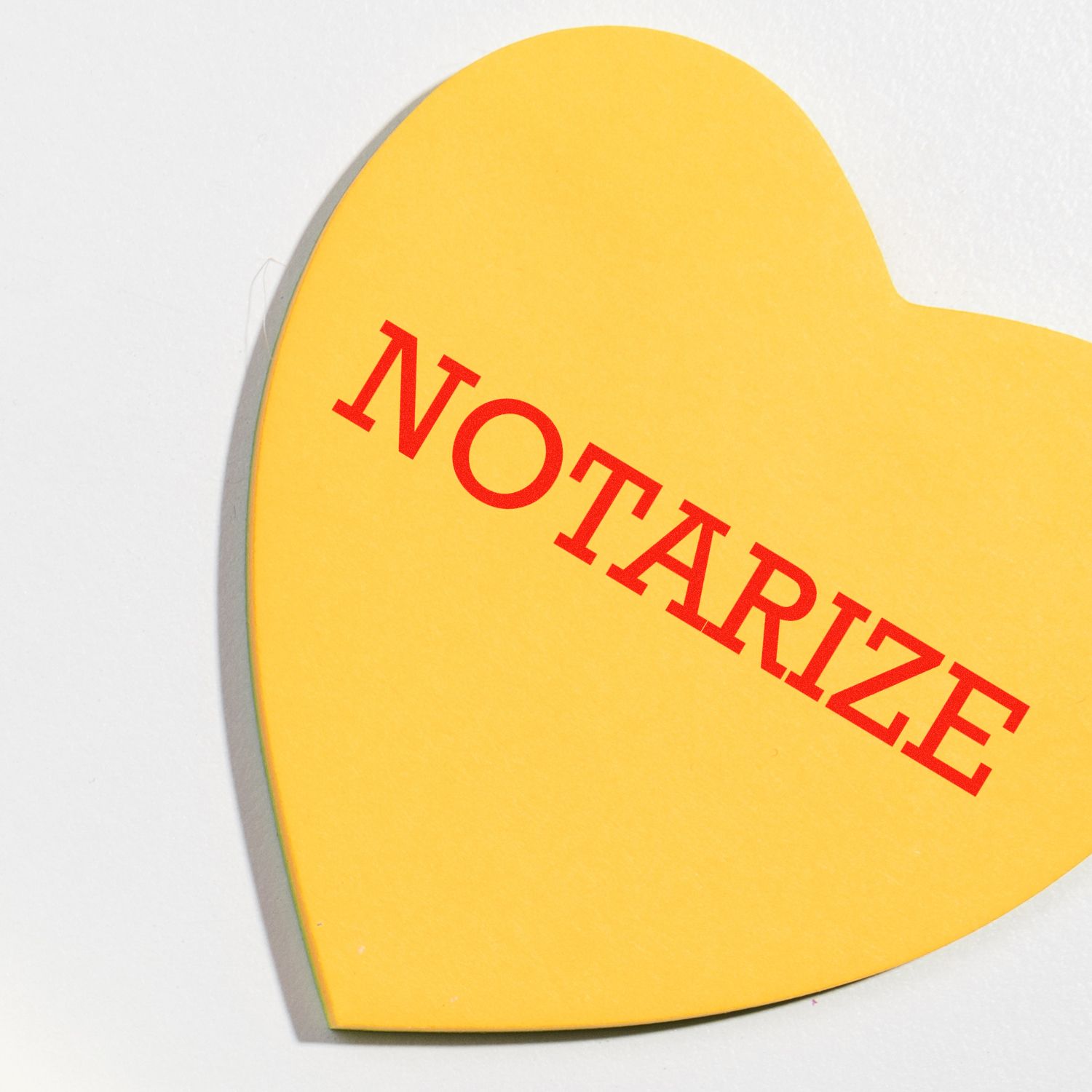 Yellow heart-shaped Large Pre-Inked Notarize Stamp with NOTARIZE in red text, placed on a white background.