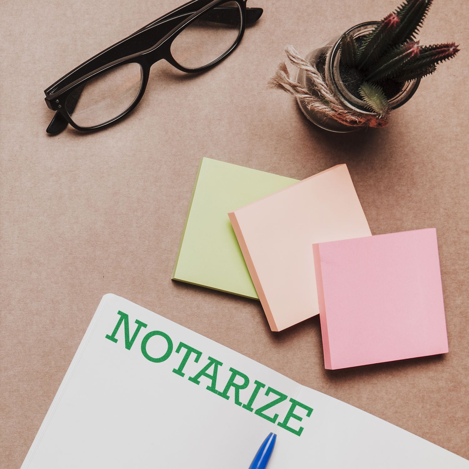 Large Pre-Inked Notarize Stamp on a desk with sticky notes, glasses, a pen, and a small potted plant.