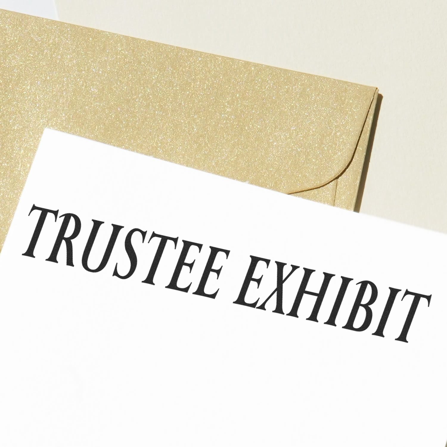 Large Pre-Inked Trustee Exhibit Stamp impression on white paper with a gold envelope in the background.