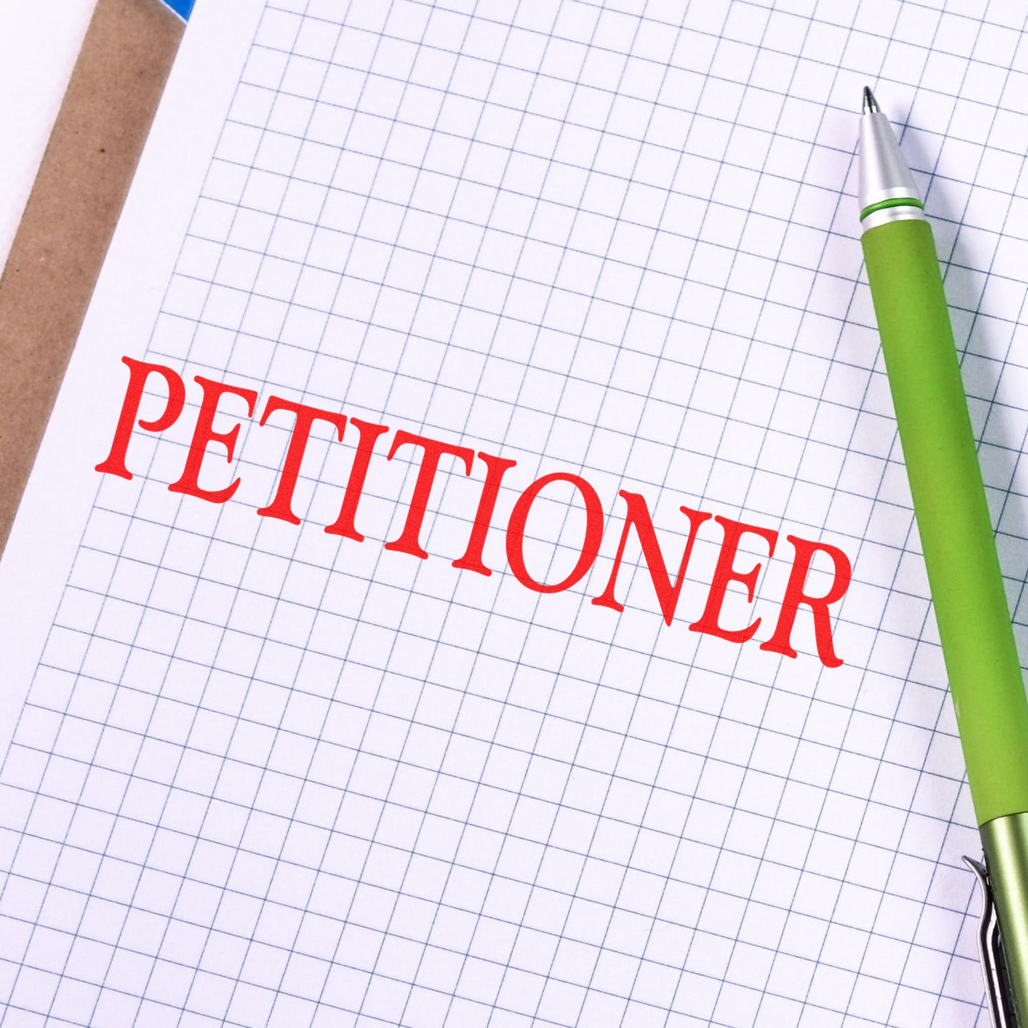 Large Pre-Inked Petitioner Stamp in red ink on graph paper with a green pen beside it.