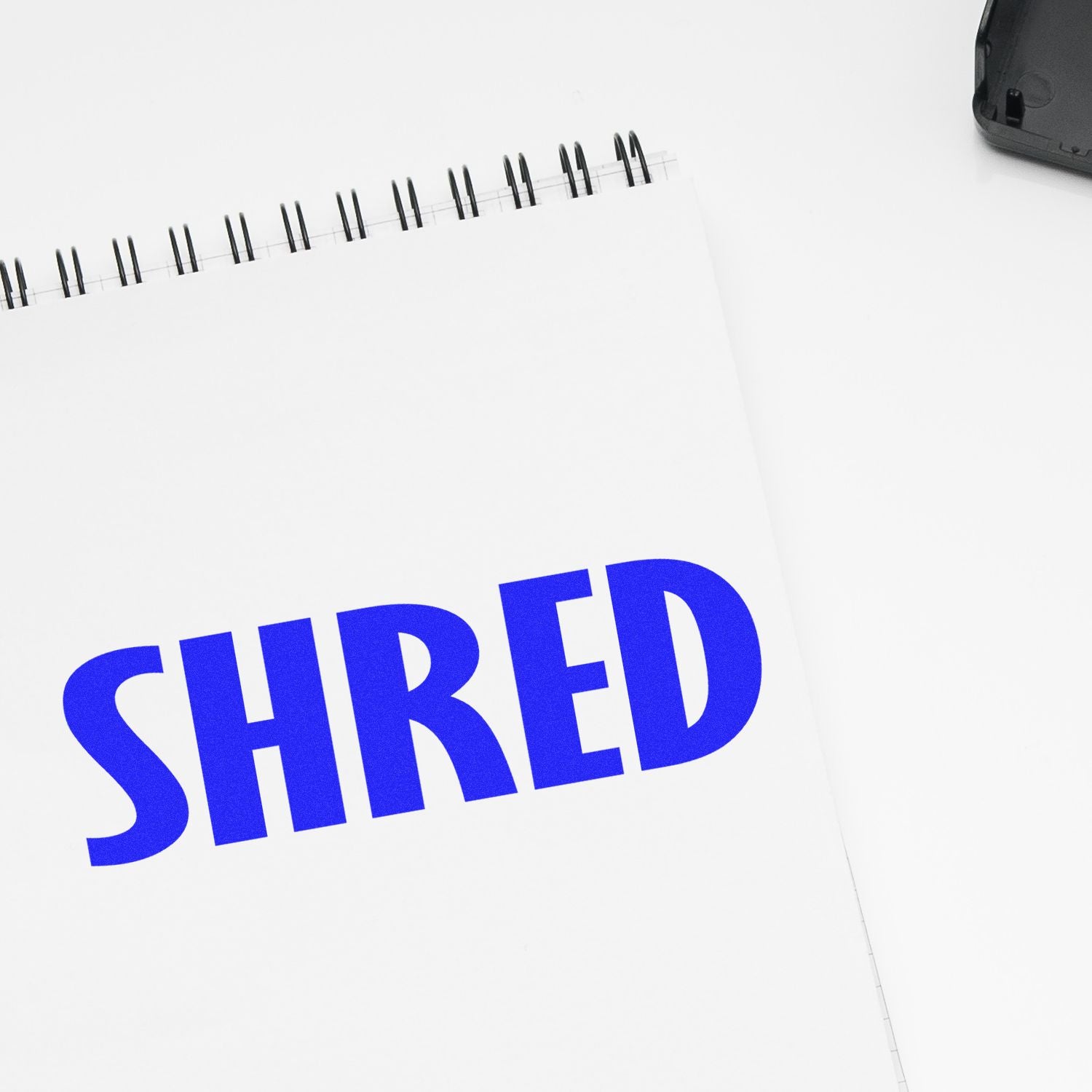 Large Pre-Inked Shred Stamp imprinting the word SHRED in bold blue letters on a white spiral notebook, with the stamp partially visible.