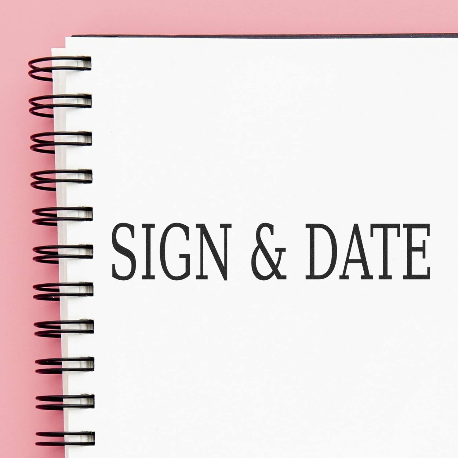 Large Pre-Inked Sign & Date Stamp on a white spiral notebook with a pink background.