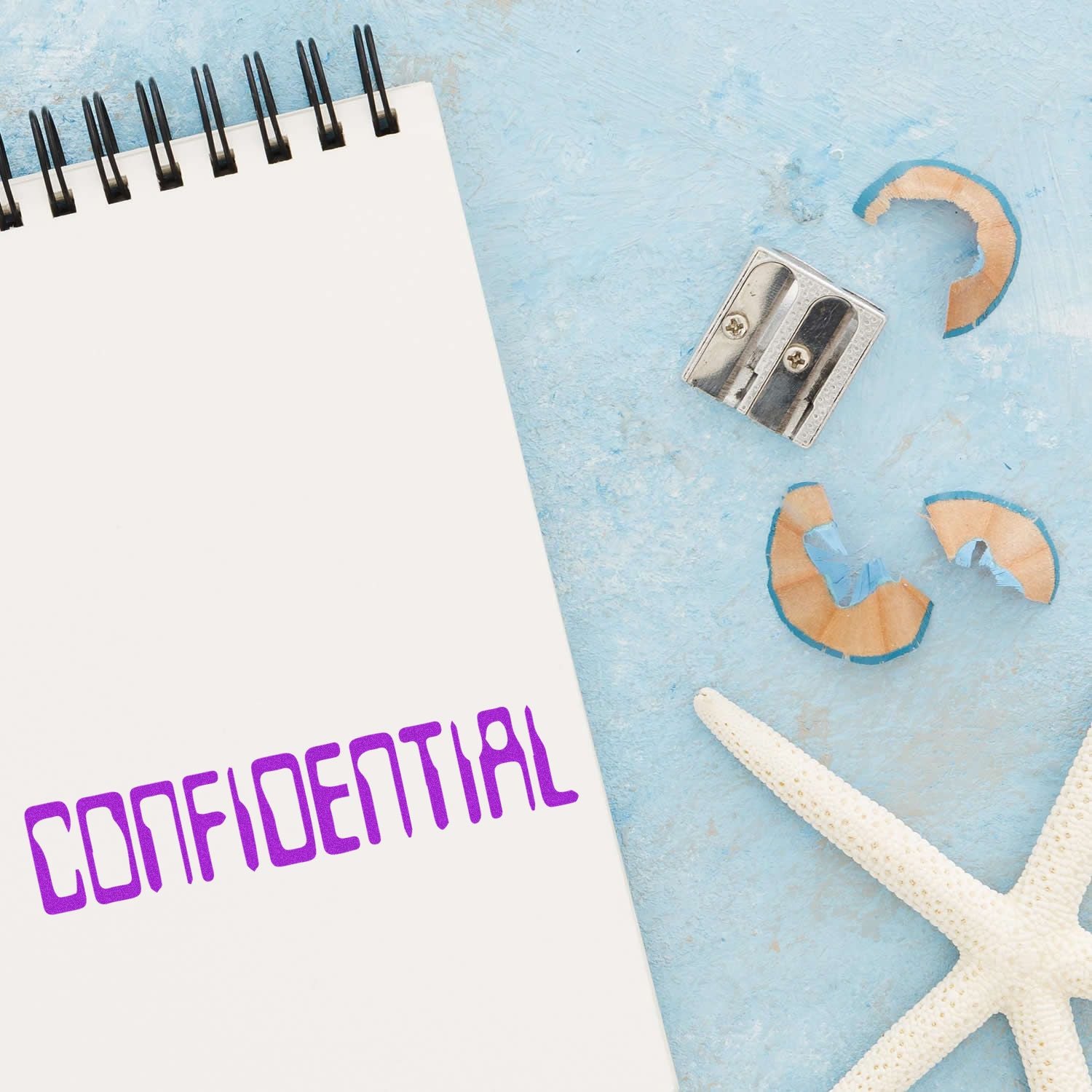 A Large Pre-Inked Barcode Confidential Stamp marks CONFIDENTIAL on a notepad, with a pencil sharpener, shavings, and a starfish nearby.