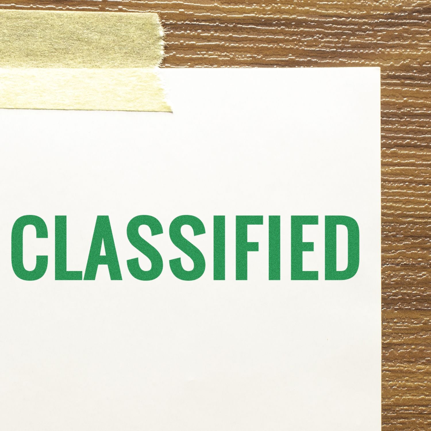 Large Pre-Inked Classified Stamp marking a white paper with the word CLASSIFIED in green, taped to a wooden surface.