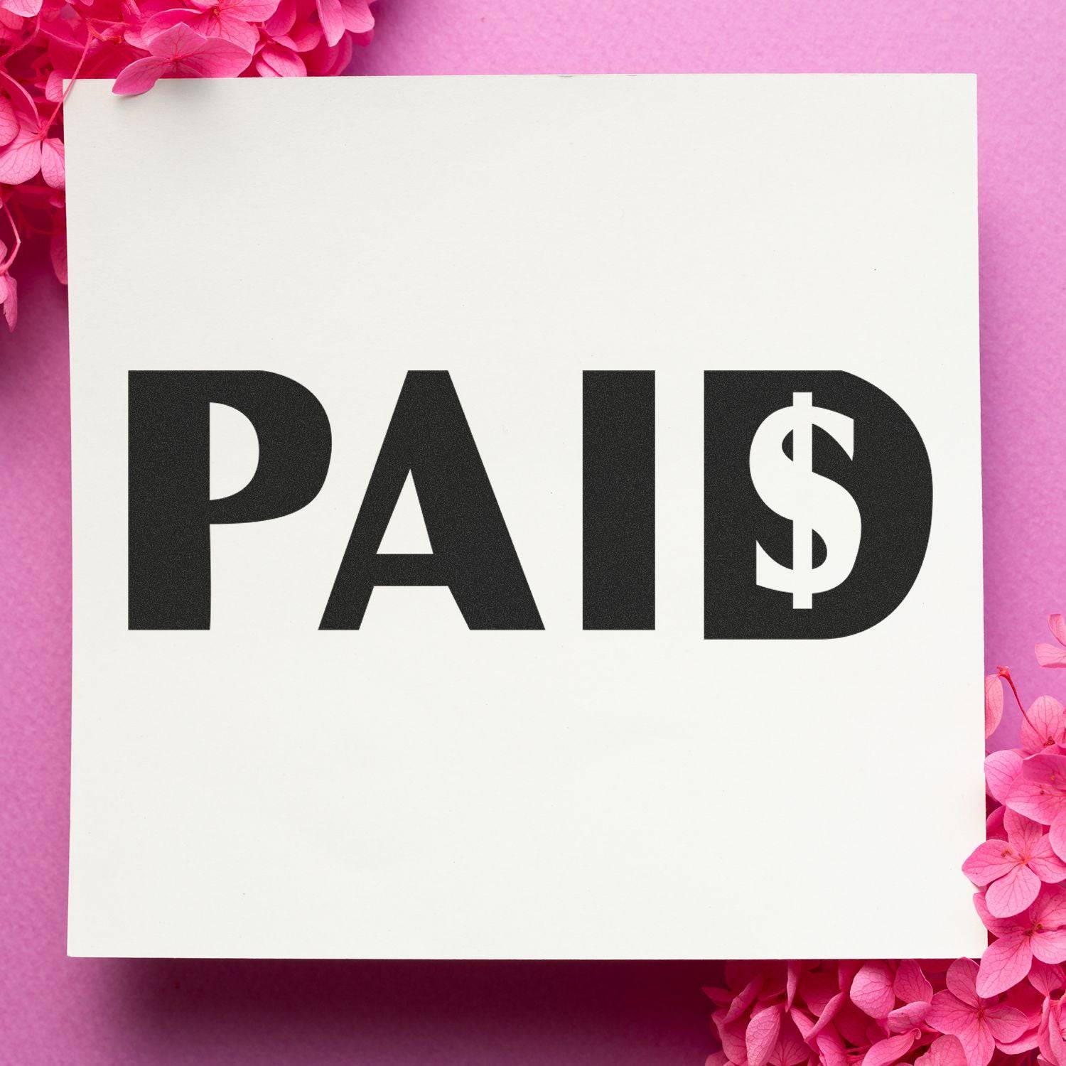 Large Pre-Inked Paid with Dollar Sign Stamp on white paper, surrounded by pink flowers, against a pink background.