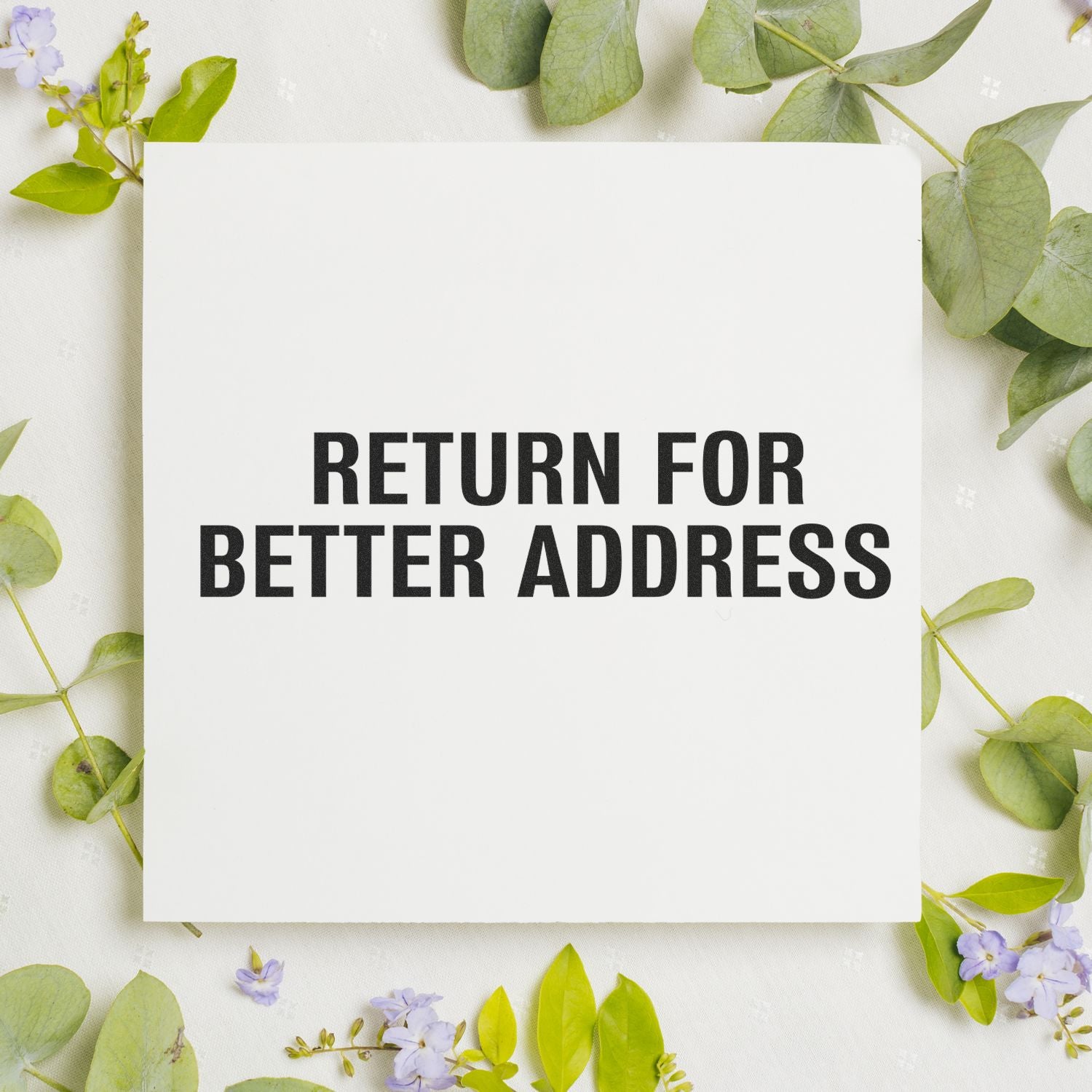 Large Pre-Inked Return for Better Address Stamp on a white card surrounded by green leaves and small purple flowers.