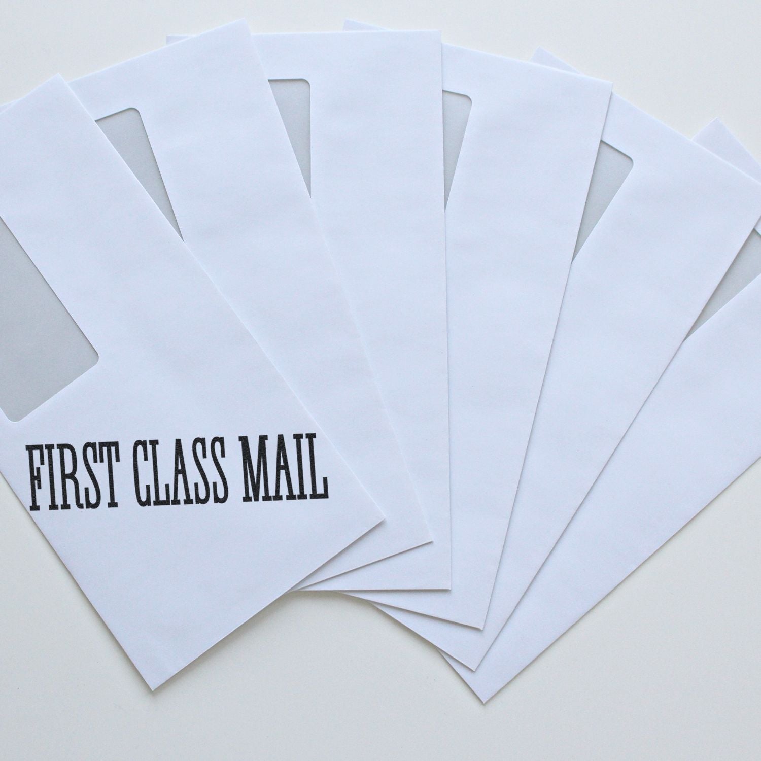 Five white envelopes stamped with FIRST CLASS MAIL using the Large Pre-Inked Times First Class Mail Stamp, arranged in a fan shape.